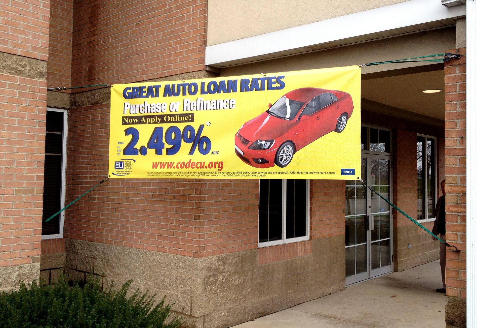 Banner offering 2.49% auto loan rates, red car graphic, yellow background. Outside brick building.