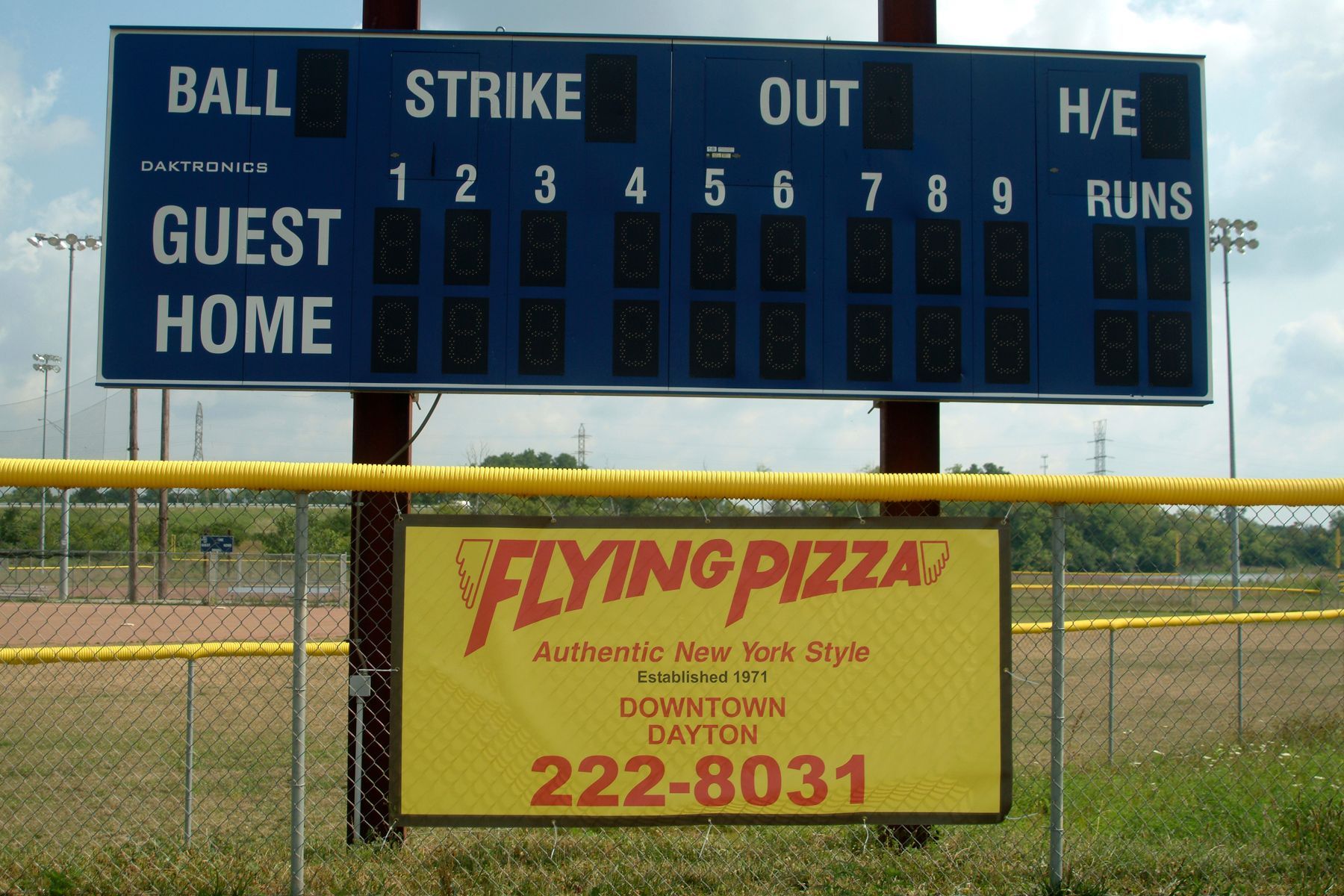Baseball scoreboard with Flying Pizza advertisement at a baseball field.