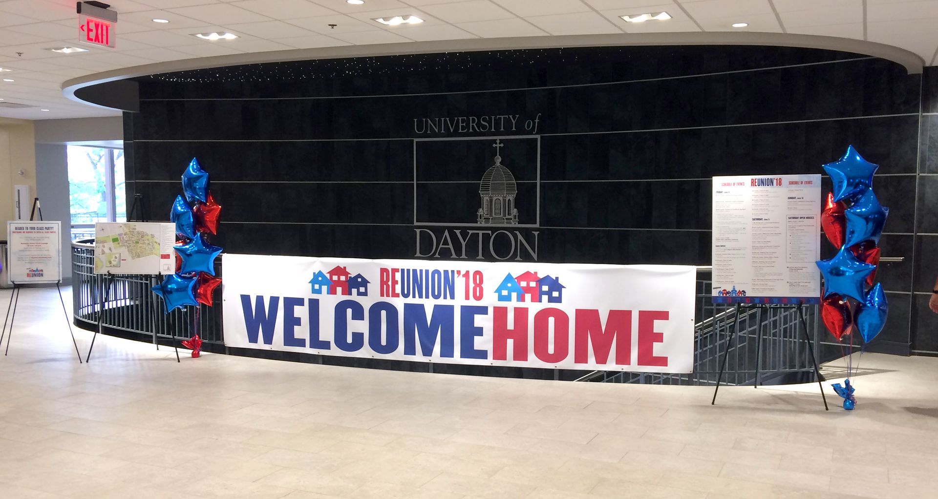 Welcome home banner at the University of Dayton reunion, with balloons and a black backdrop.