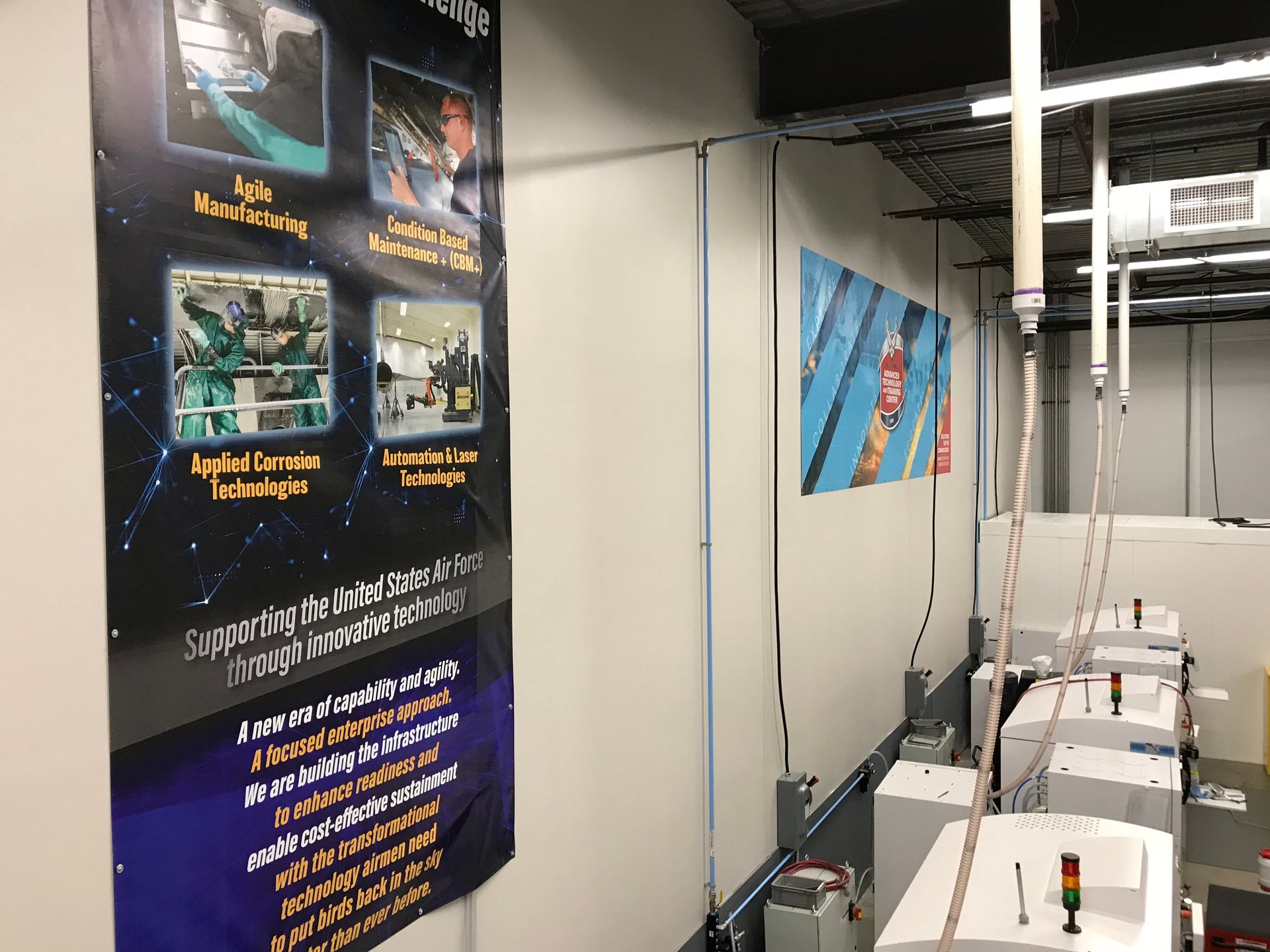 Banner and equipment in a lab setting. Banner has text, images. Equipment is white, with red lights.