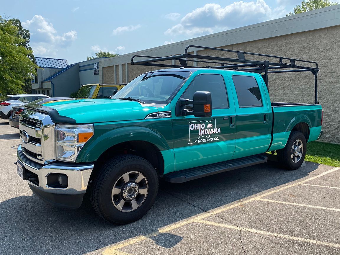 Green pickup truck with a black roof rack parked in a lot on a sunny day.