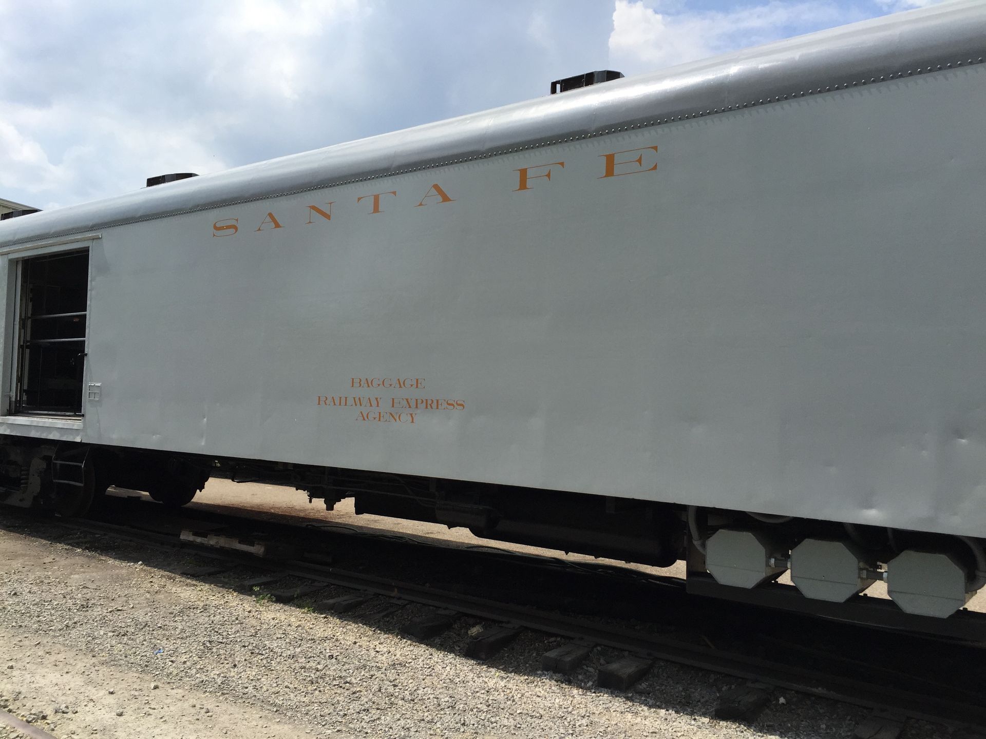 Side view of a silver Santa Fe train car with orange lettering, parked on train tracks.