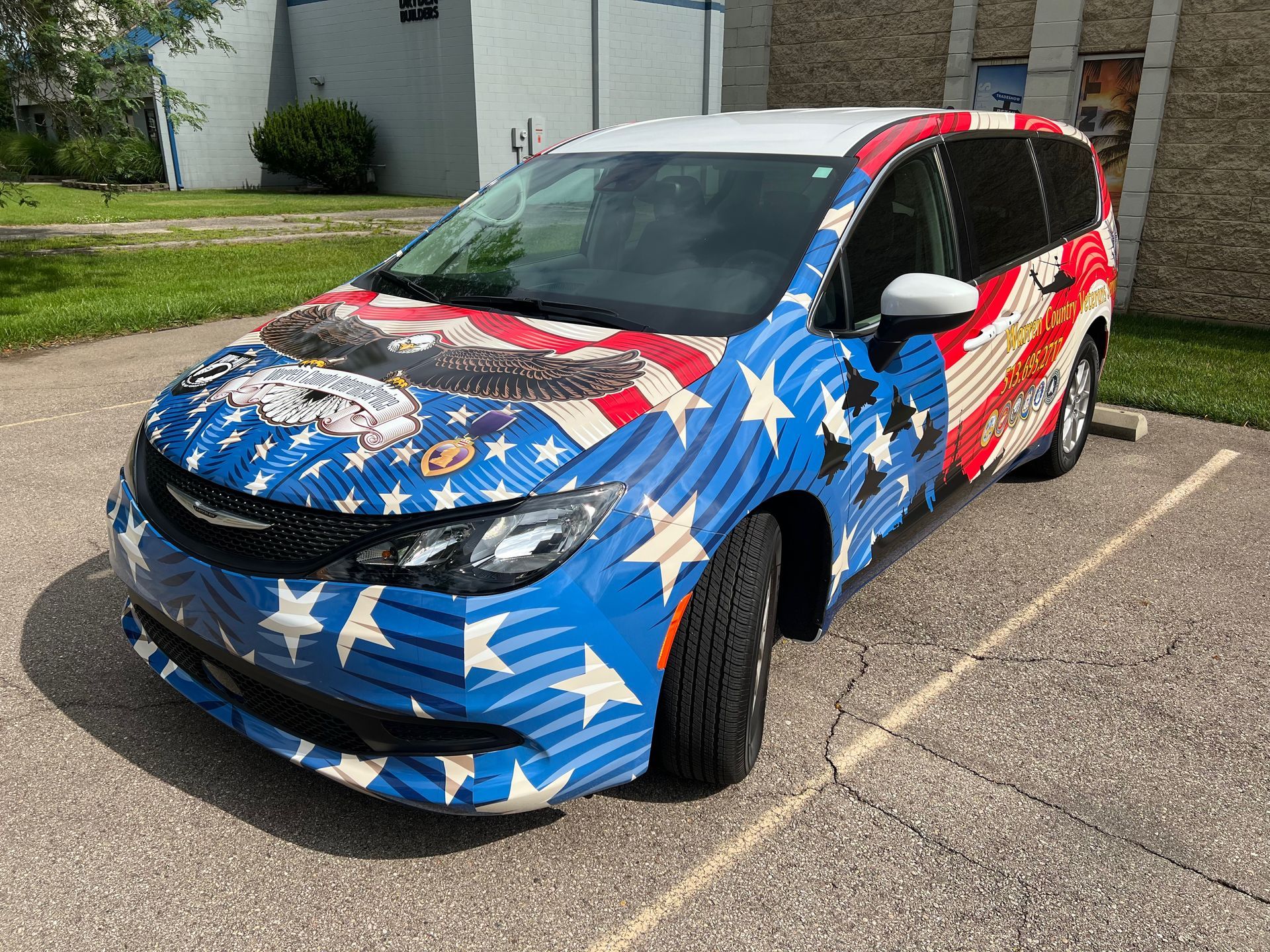 Minivan wrapped in American flag design, parked outside, under a sunny sky.