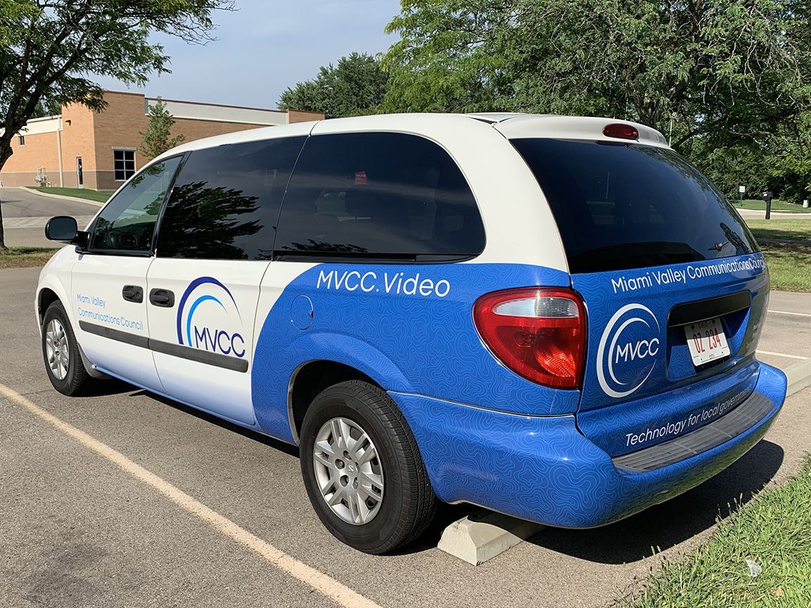 Blue and white MVCC Video van parked outdoors on a sunny day. The van has logos and writing on its sides.