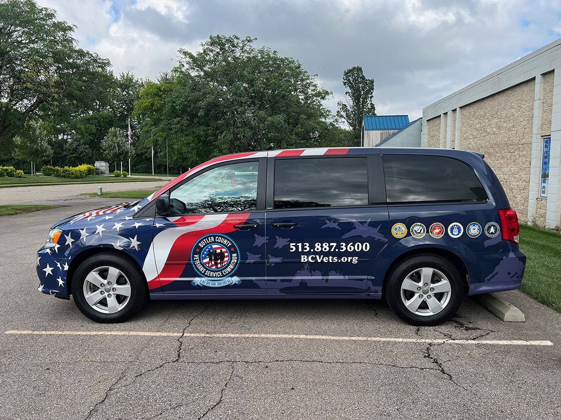 Van with US flag design and veteran service logos. Dark blue with patriotic colors parked outdoors.