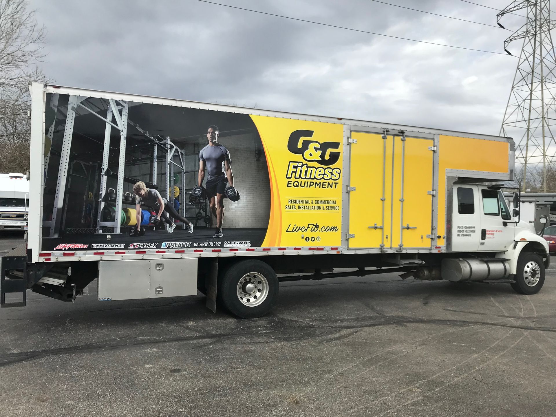 A large truck with a fitness equipment advertisement on the side in front of an outdoor setting.