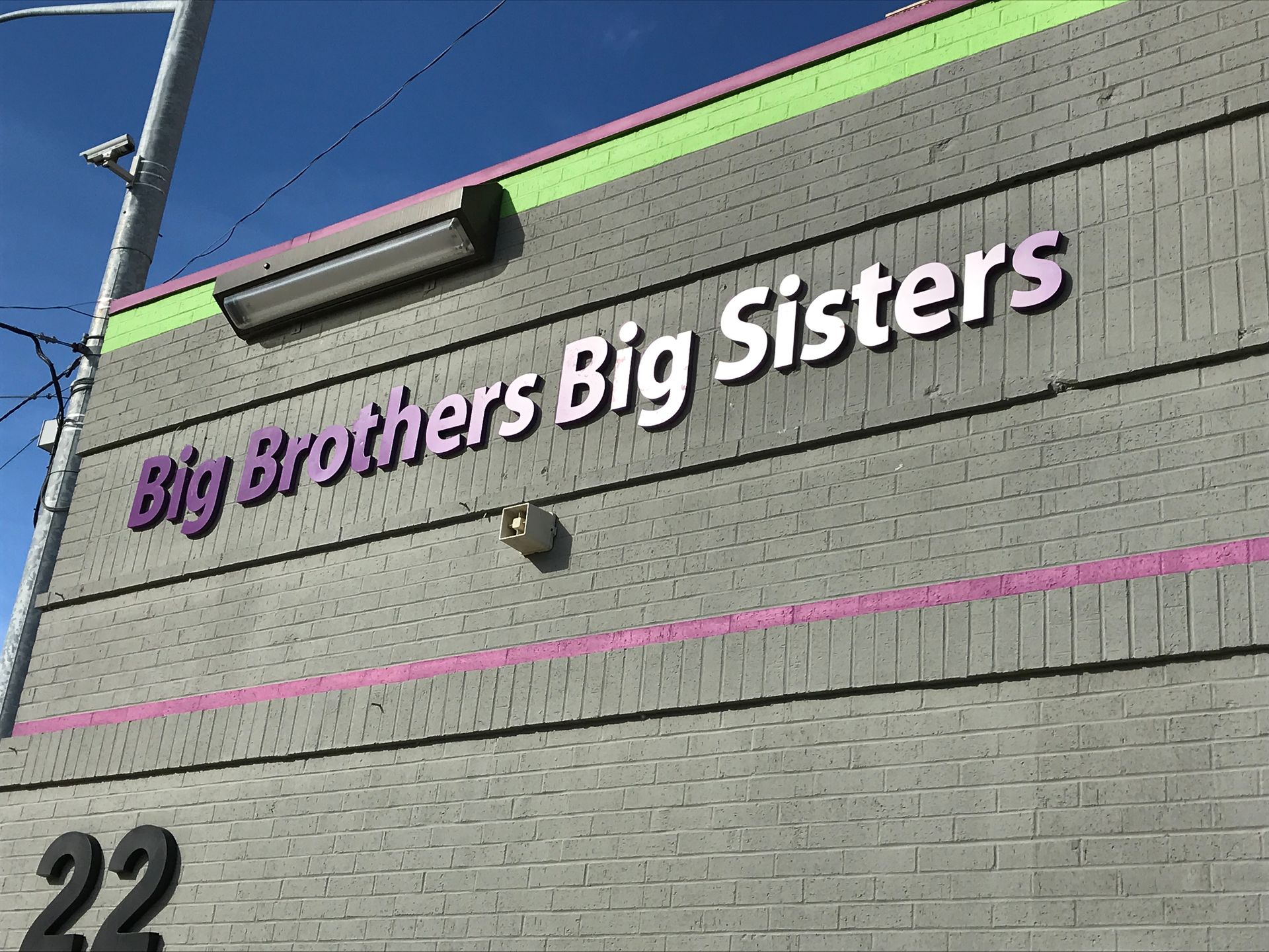 Big Brothers Big Sisters sign on a gray brick building, purple lettering, green and pink trim.