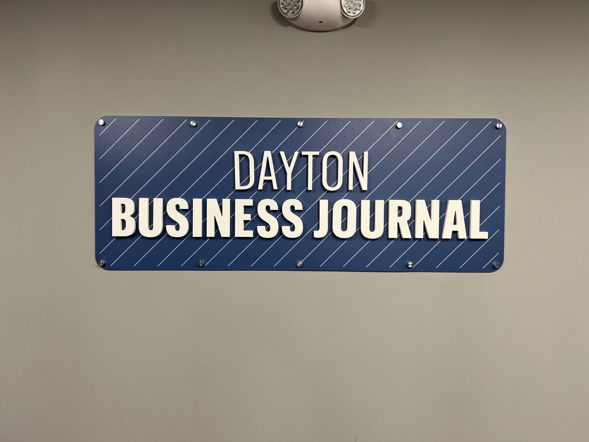 Dayton Business Journal sign on a blue background, mounted on a gray wall.