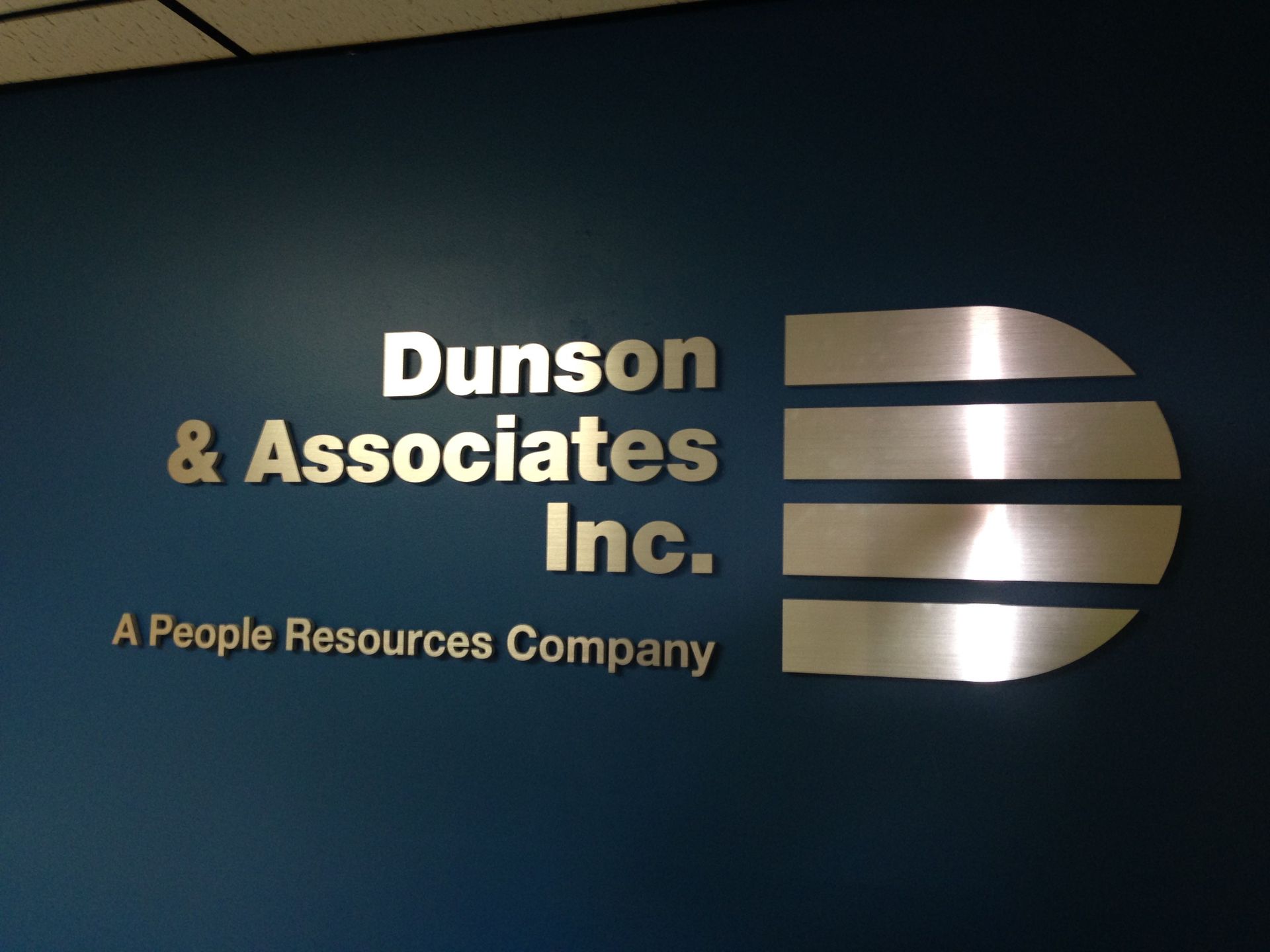 Logo for Dunson & Associates Inc. on a blue wall: silver text reads name with a stylized 