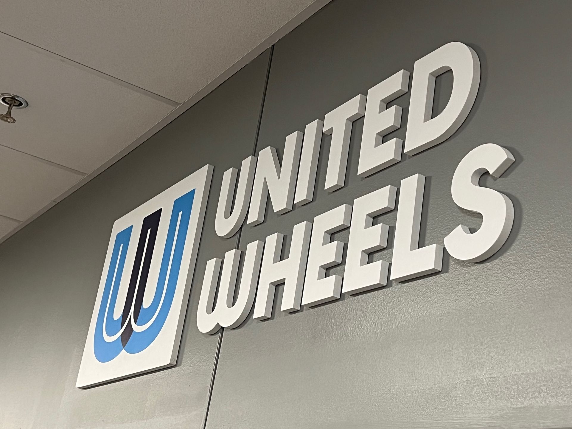United Wheels logo on gray wall: blue and white 