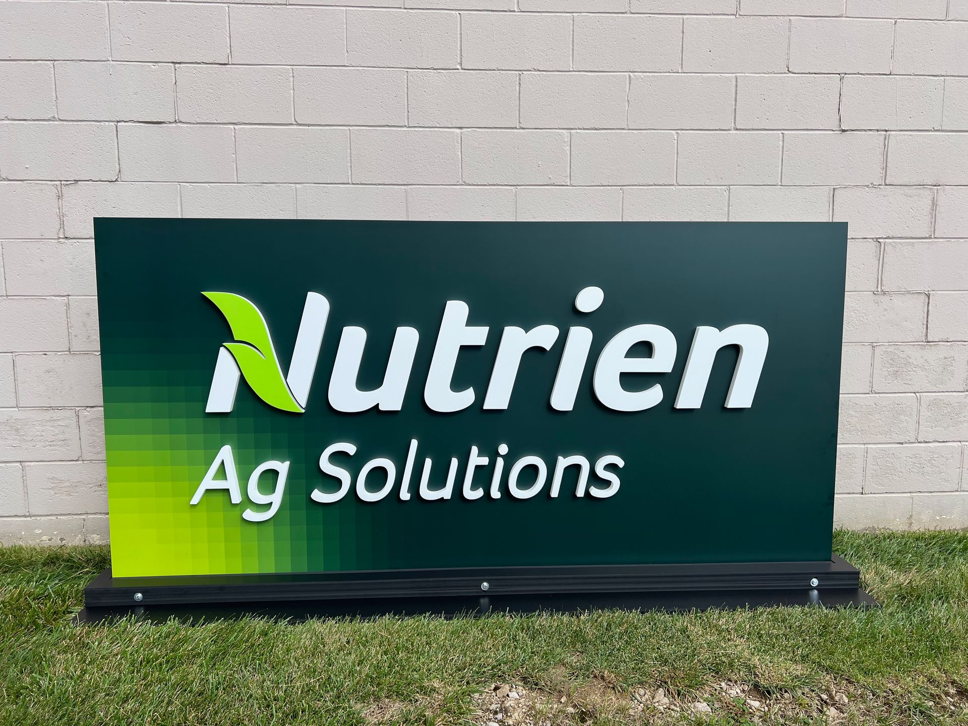Nutrien Ag Solutions sign with green gradient background and white text, on a grass surface.