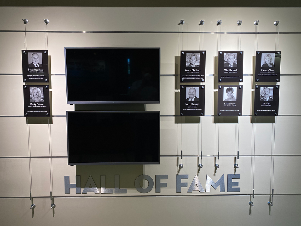 Wall display with Hall of Fame sign, photos, and two black screens.