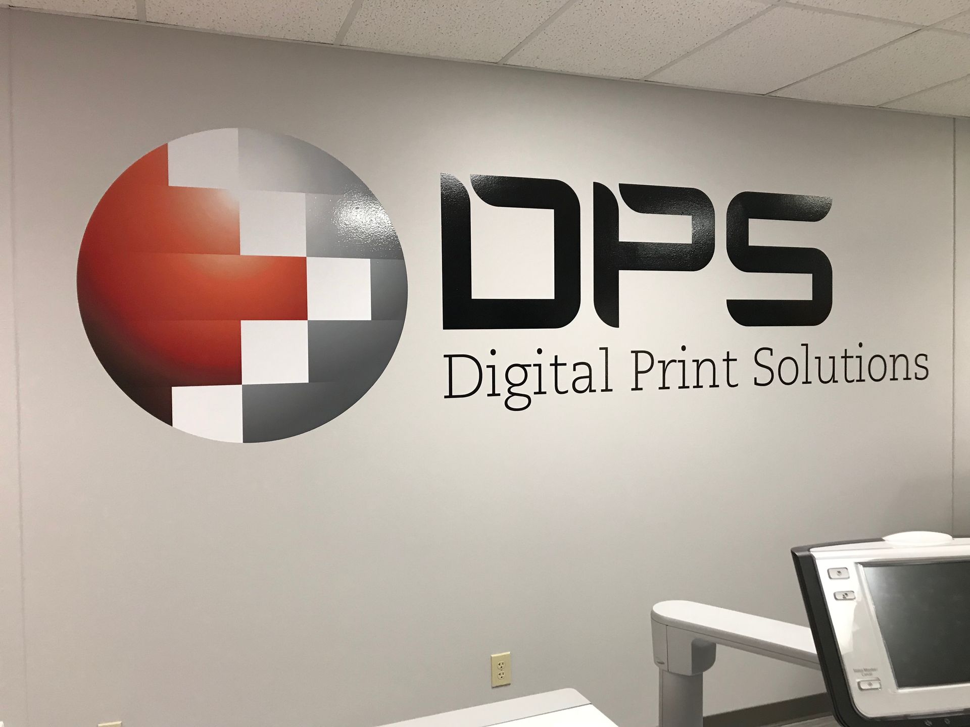 Logo for Digital Print Solutions, on an office wall, featuring a red, white, and gray circle and black lettering.