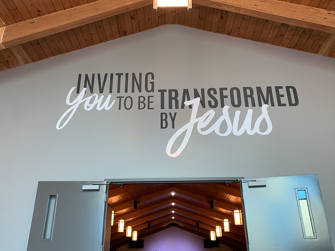 Wall inscription above church doors reads, “Inviting you to be transformed by Jesus.