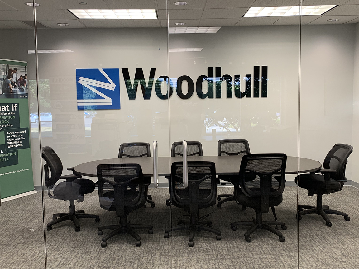 Conference room with large oval table and chairs; Woodhull logo on glass wall.