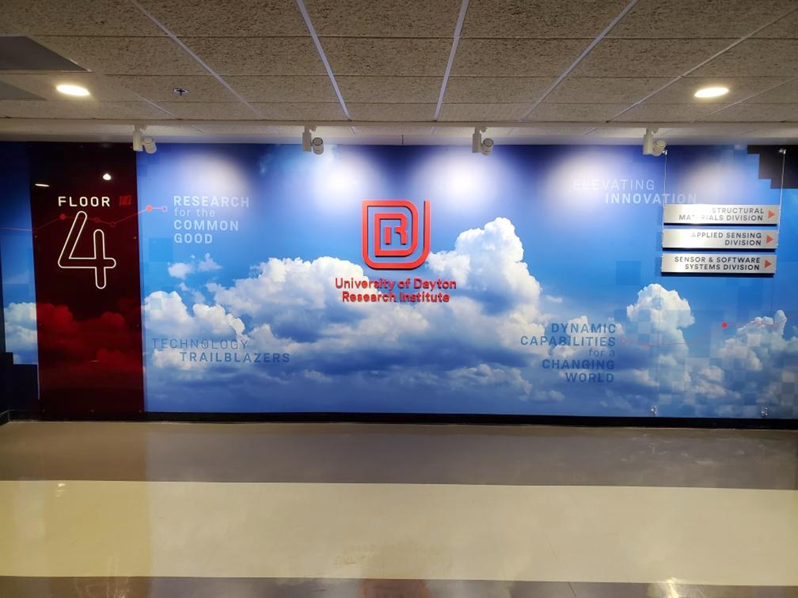 Wall mural on the 4th floor, a cloudy sky backdrop with a company logo and directional signs.
