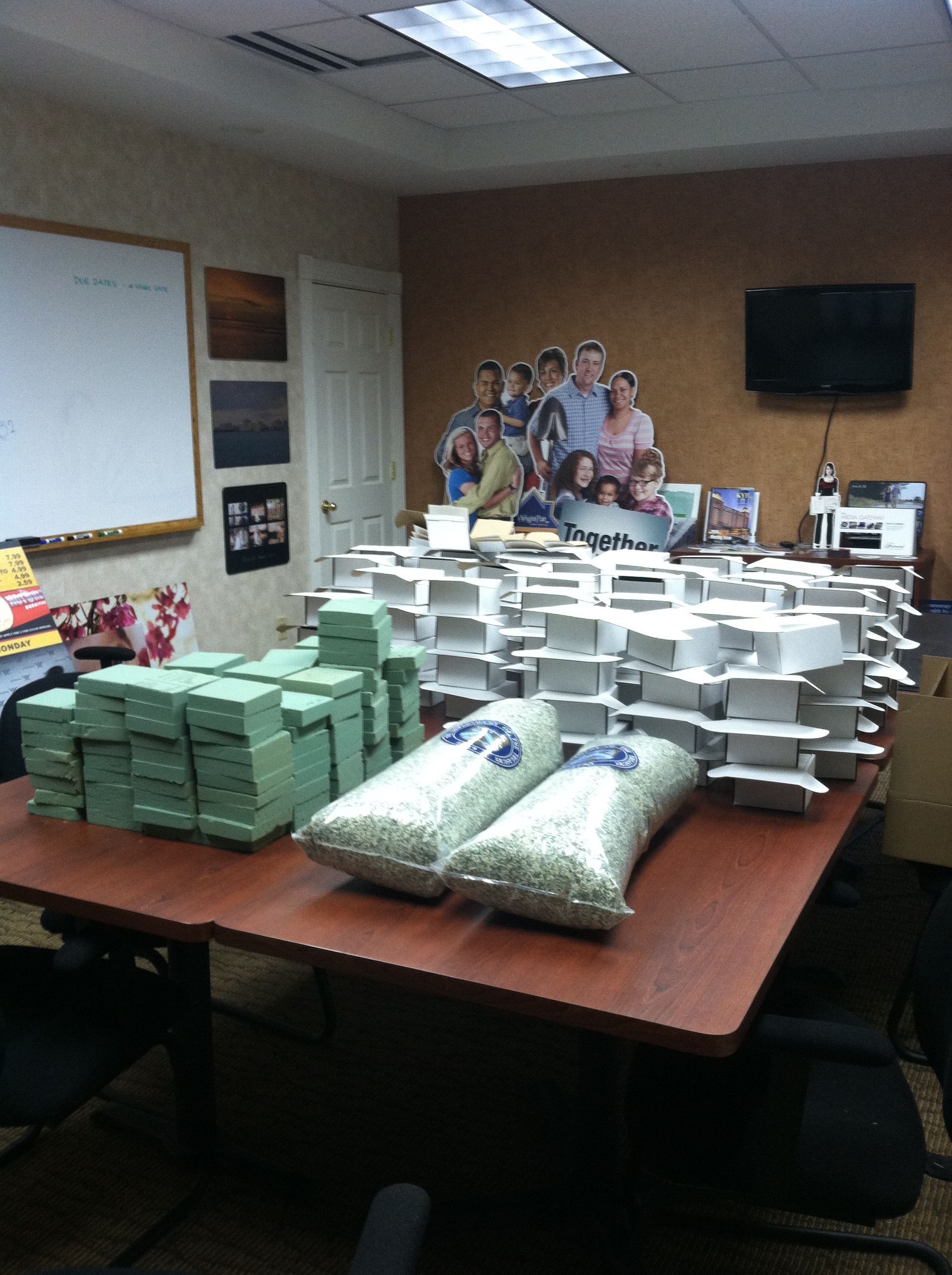 Stacks of green money, white boxes, and two bags on a table in an office with a family photo display.