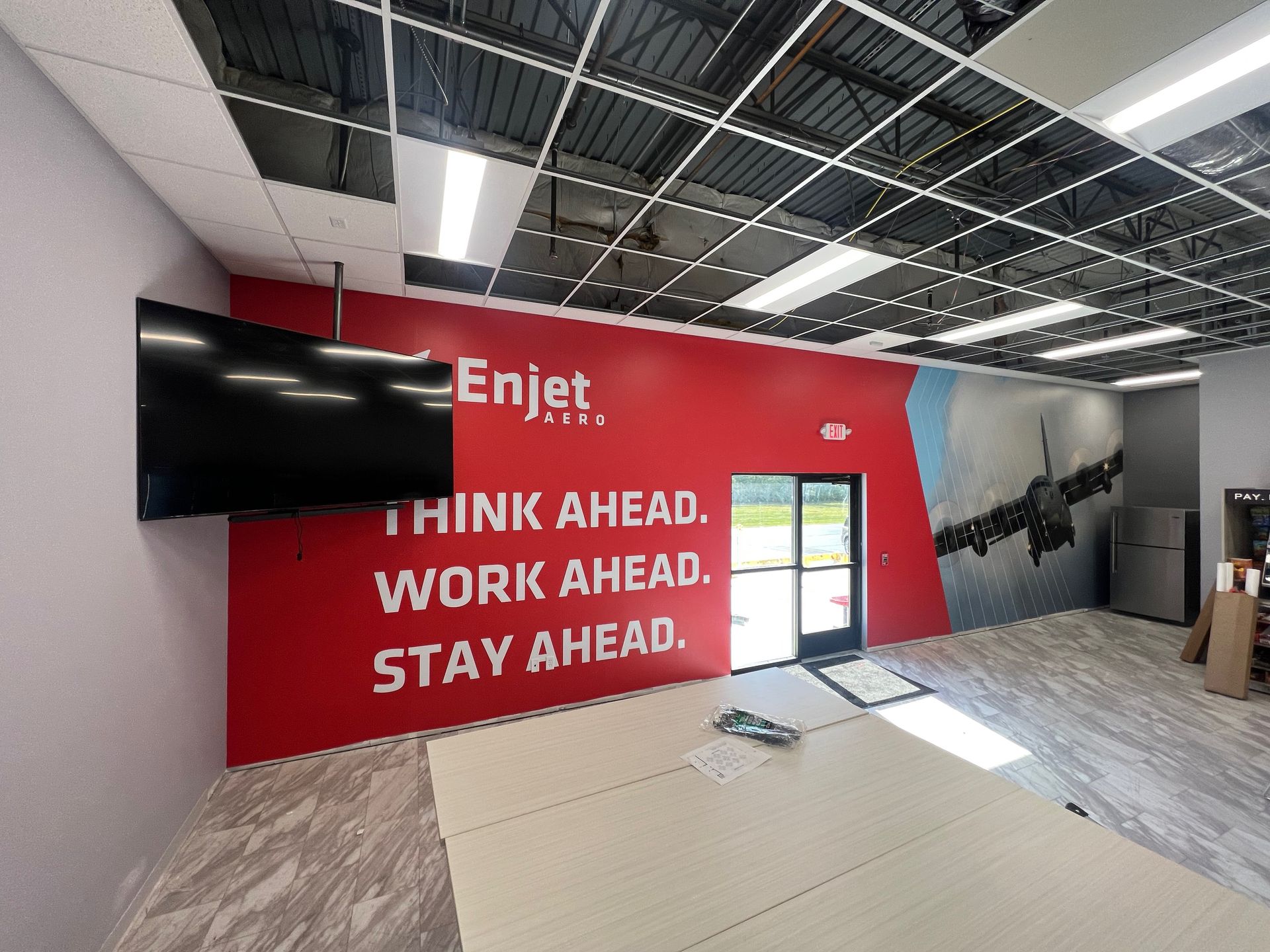 Interior office space with red accent wall, large screen, company logo and slogan, and a partially open doorway.