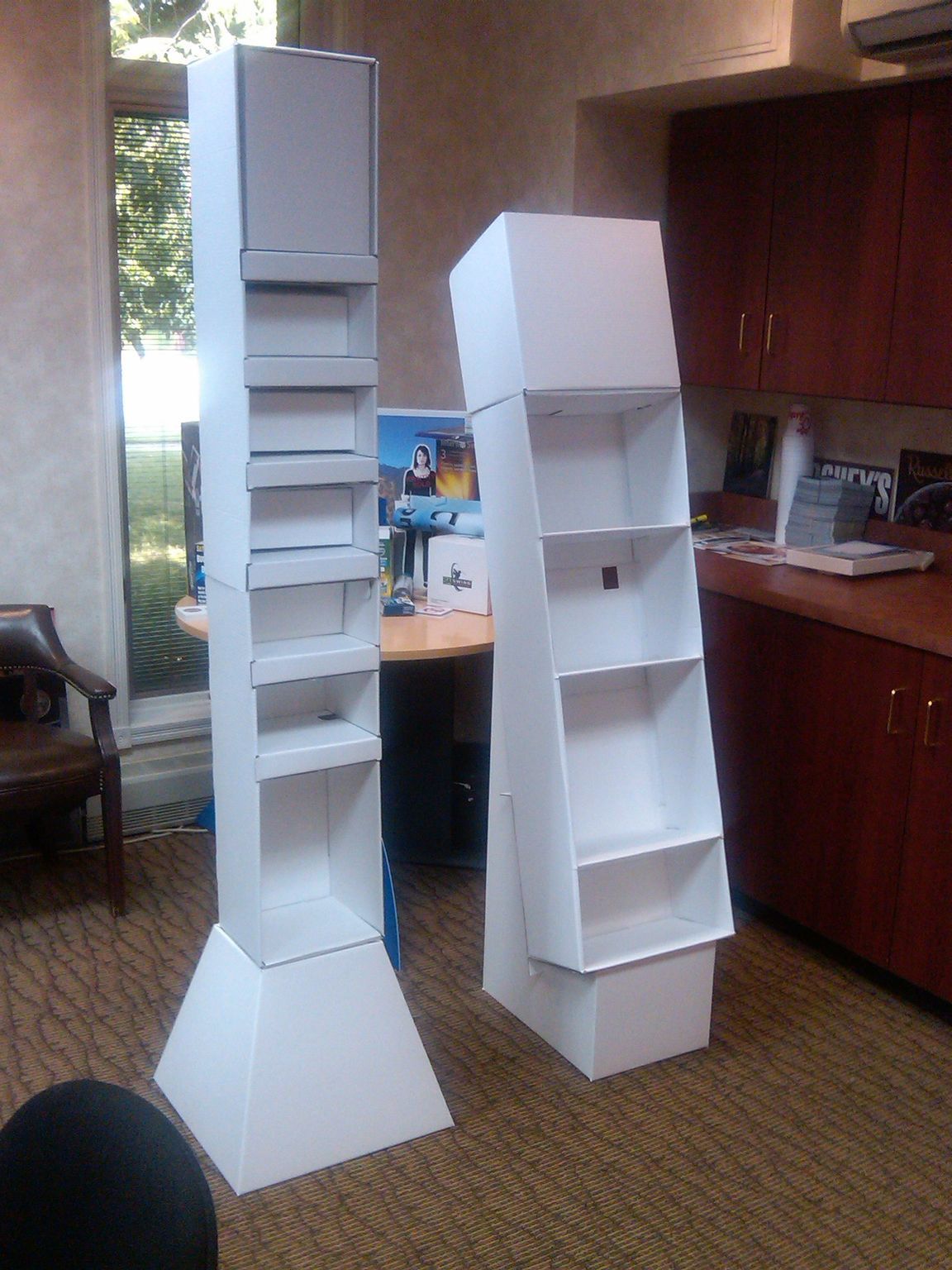 Two white cardboard display stands inside a room, one tall and rectangular, the other shorter and wider.