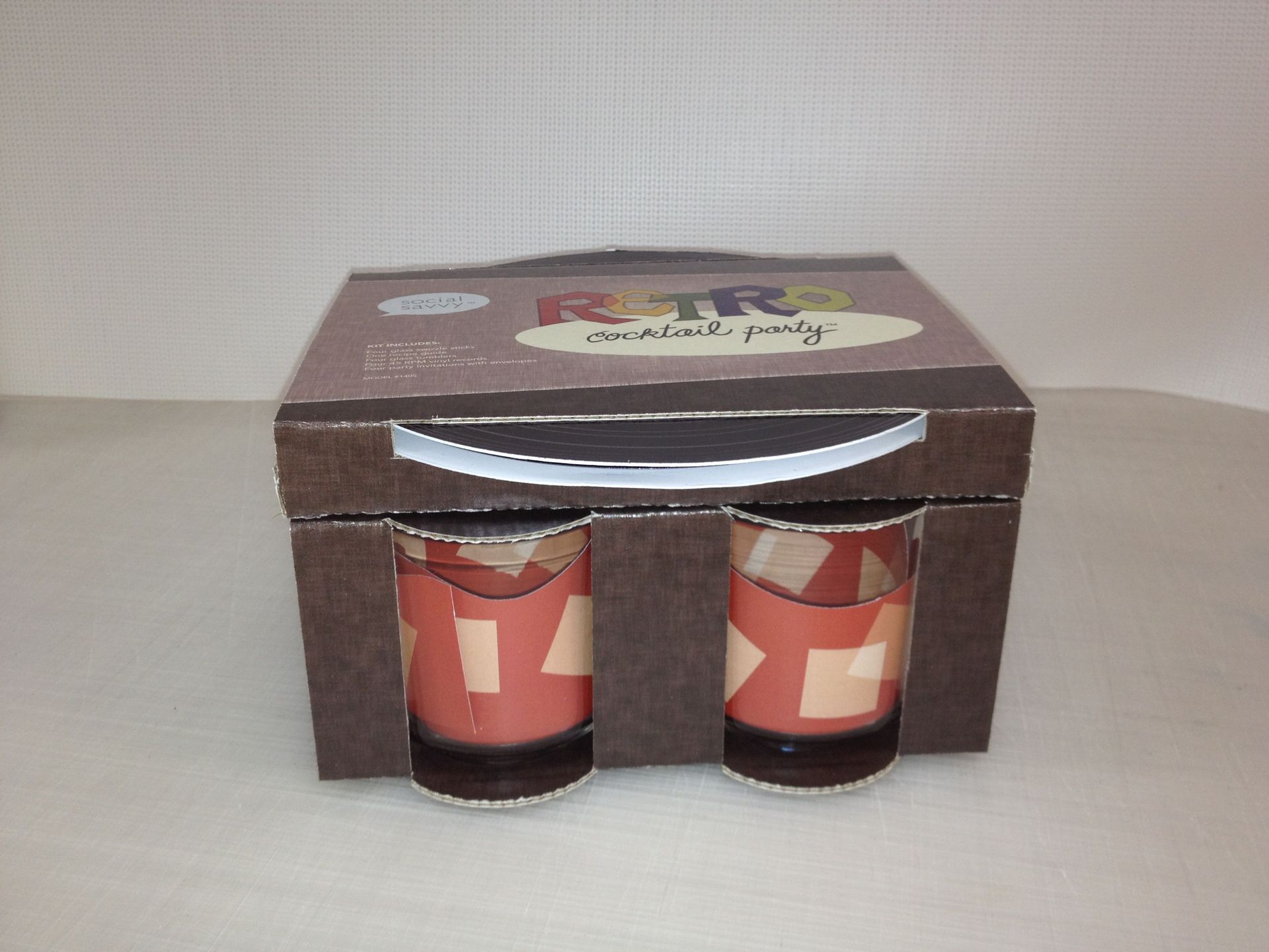 Box with handle, holds two retro-patterned drinking glasses. Brown packaging, beige and brown glasses.