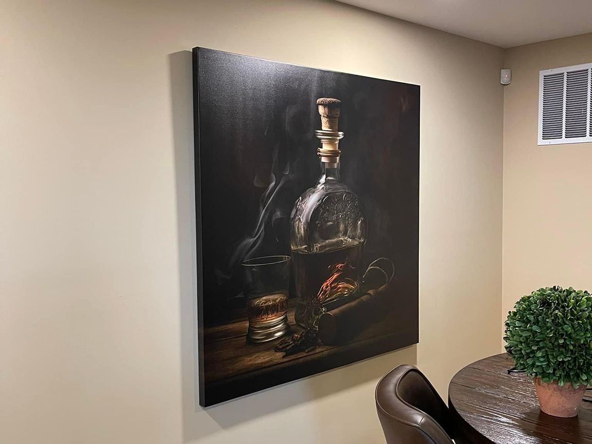 Canvas art of a liquor bottle and glass on a wooden table, mounted on a beige wall.