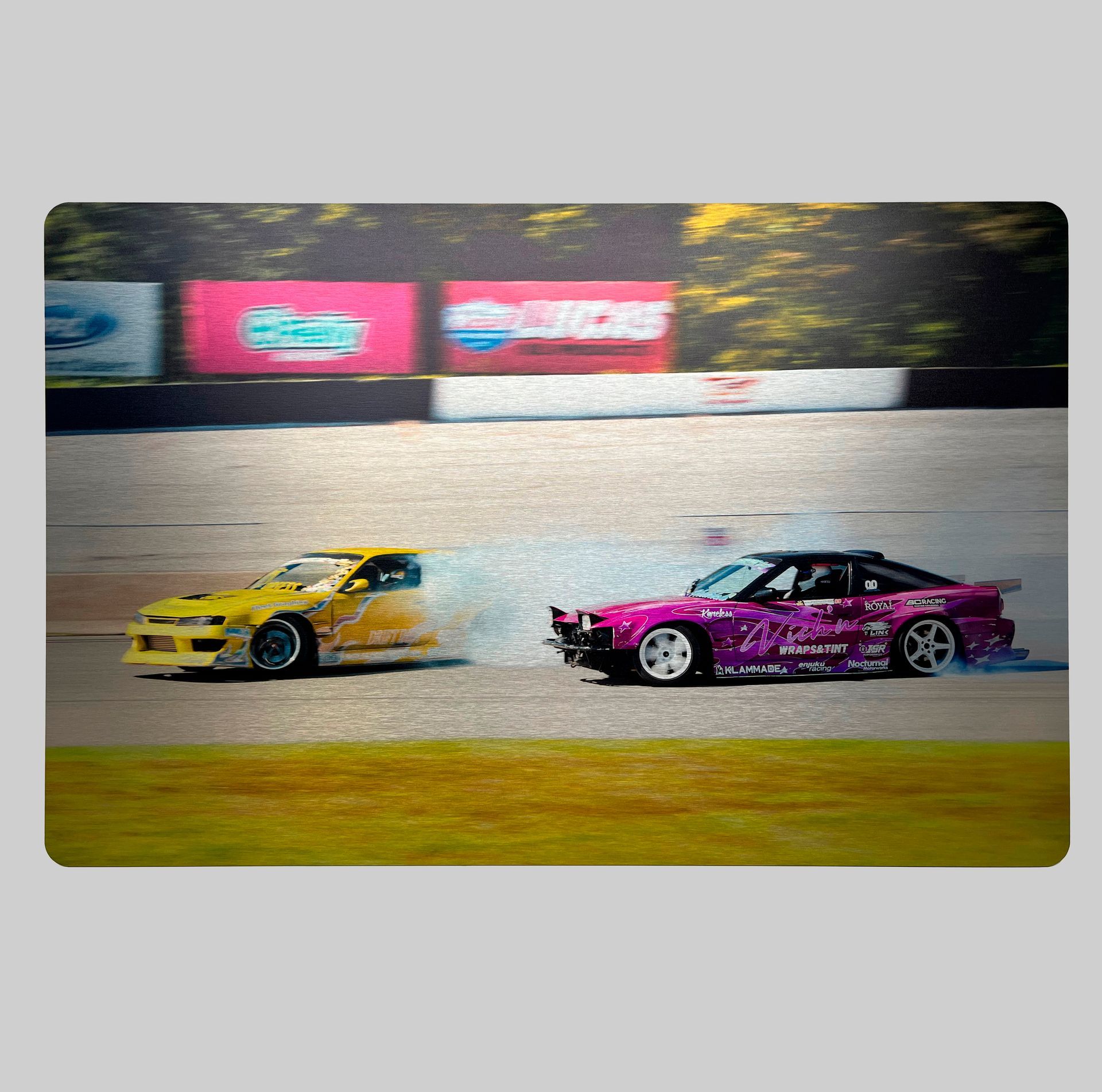 Two drifting cars, yellow and purple, on a racetrack, smoke billowing.