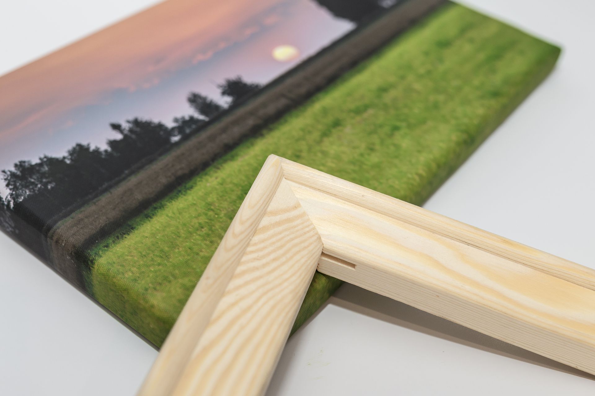Close-up of a canvas print with a wooden frame. Shows a landscape scene with a sunset over a field.