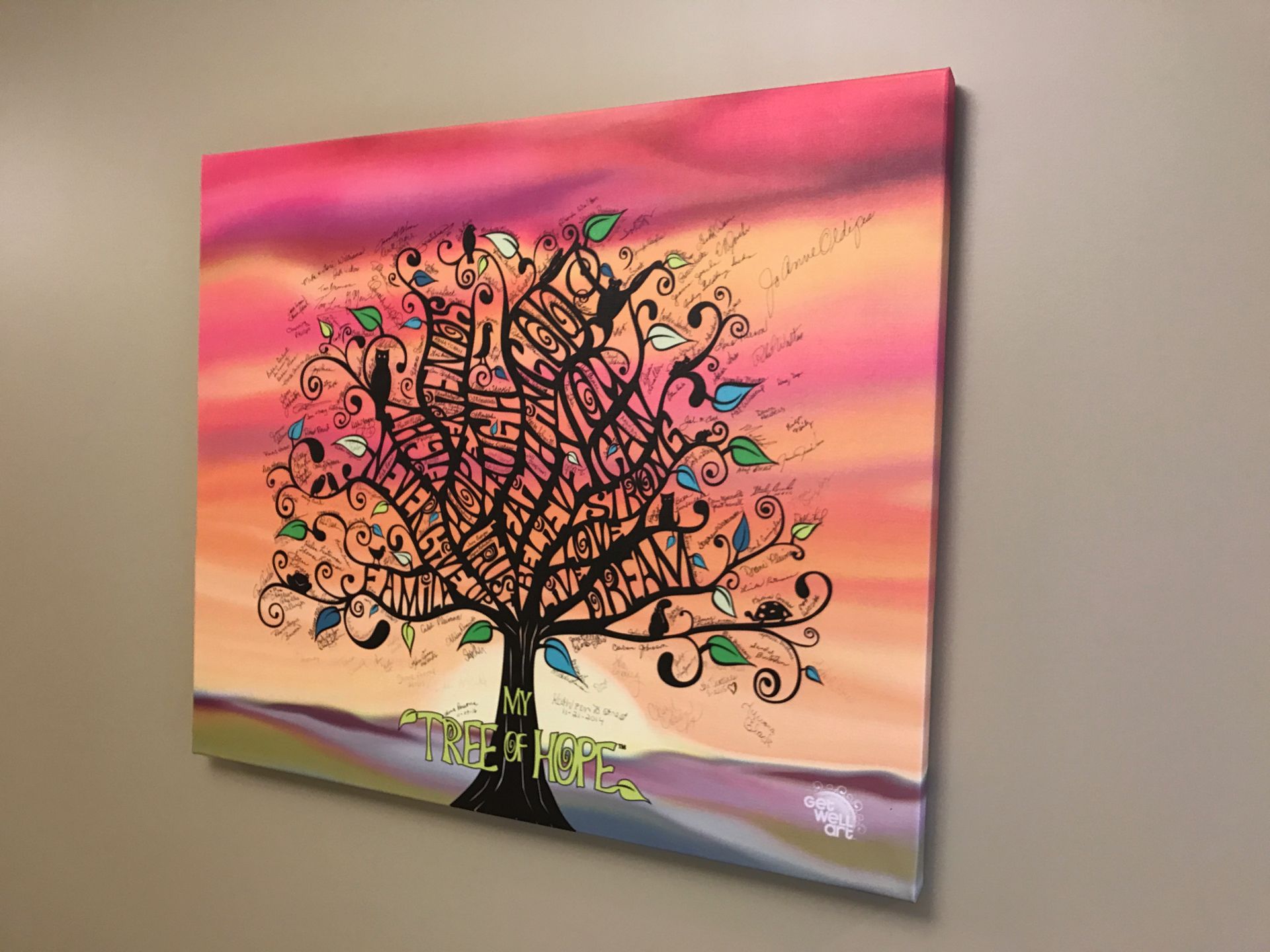 Colorful tree painting on a wall. Pink and orange sky, black tree silhouette, green leaves, stylized and whimsical.