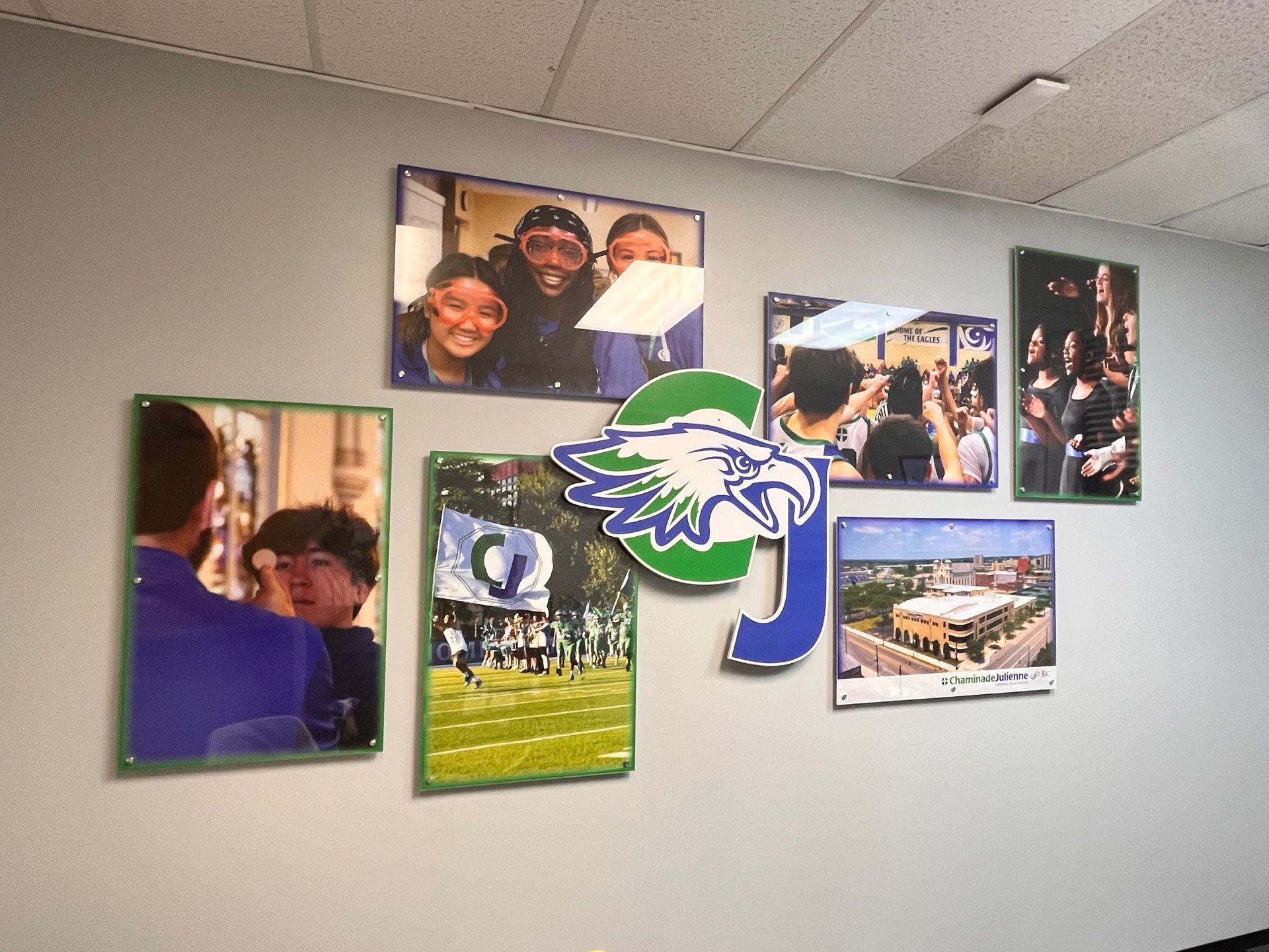 Photos and a school logo displayed on a gray wall. Includes students, a sports field, and a building.