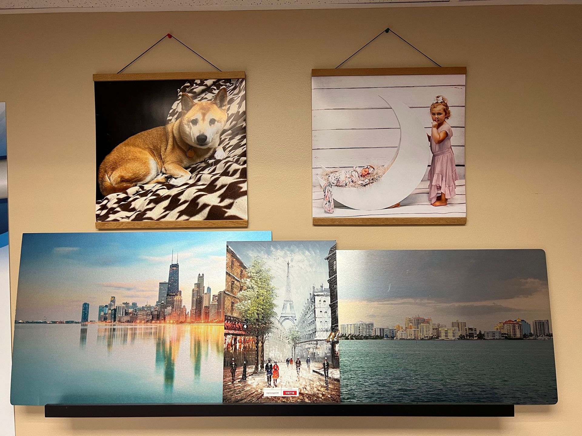 Wall art display: dog portrait, baby on crescent moon, cityscapes, all on a neutral wall.