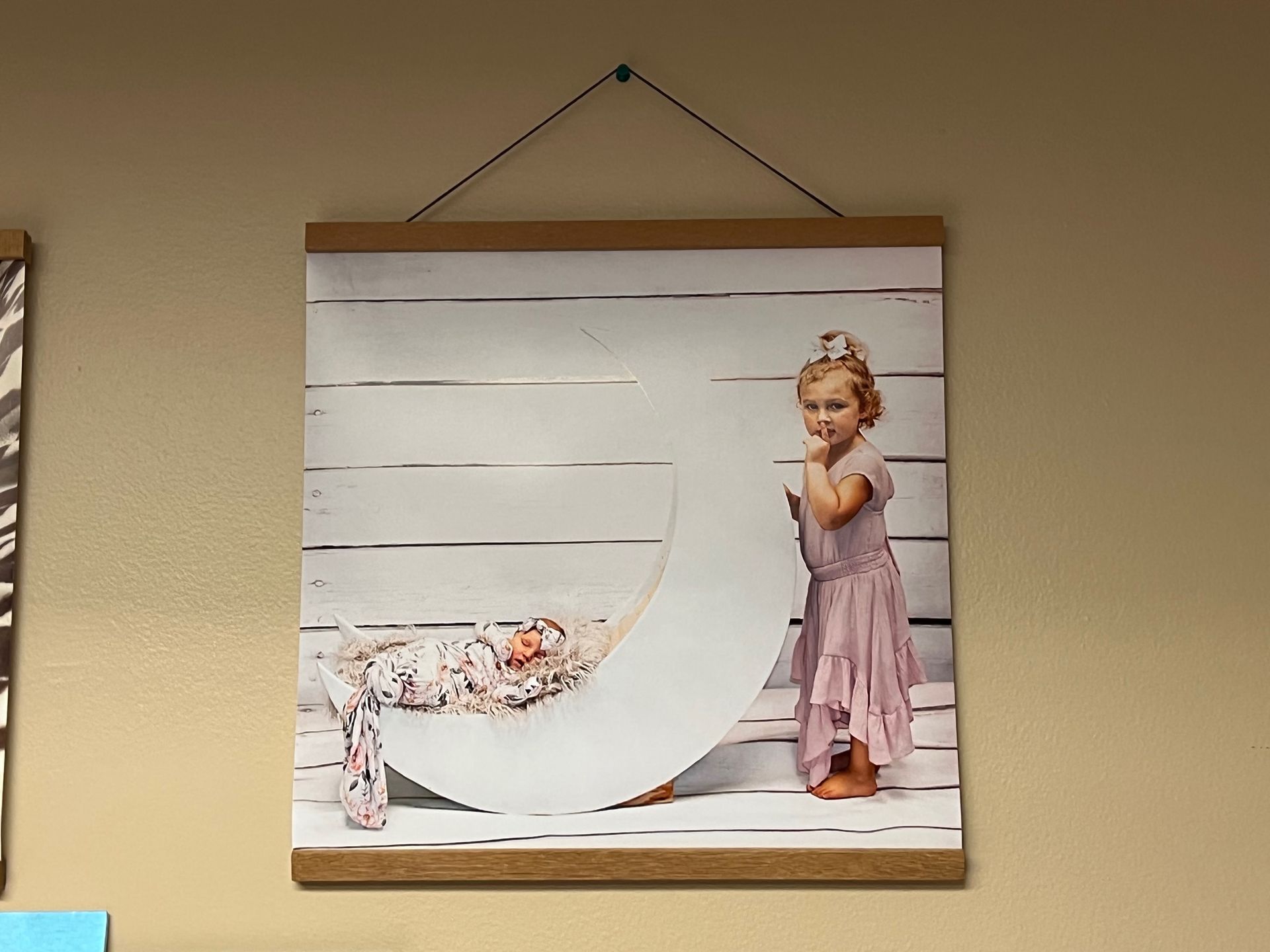 Child in pink dress standing next to a baby in a white crescent moon prop, against a white wood backdrop.