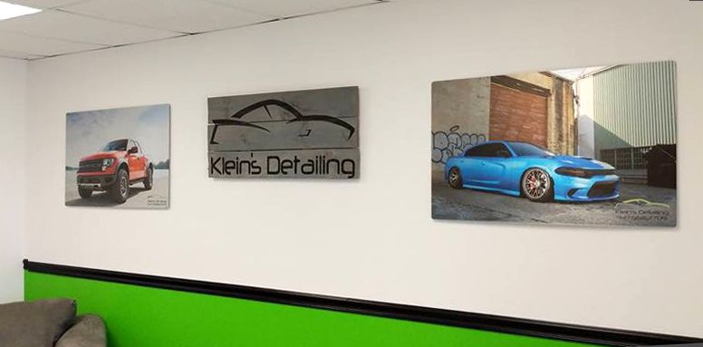 Three pictures of cars on a white wall in a shop; a car detailing sign is in the middle.