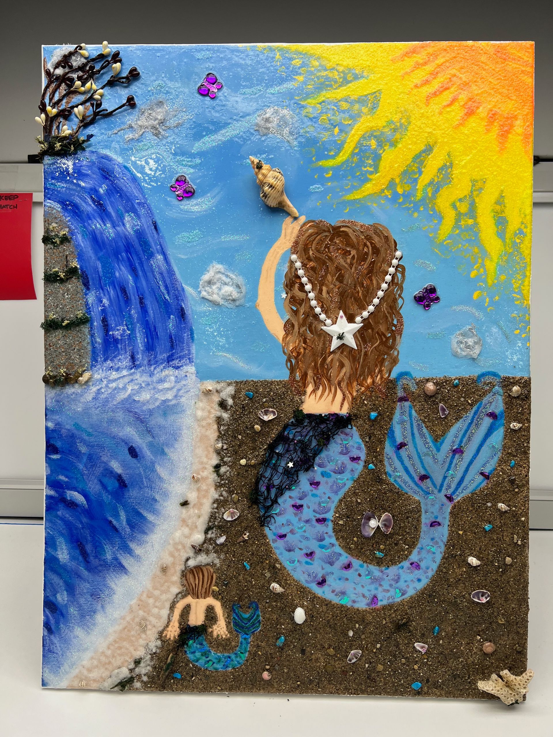 Mermaid artwork: A blue-tailed mermaid sits by the sea, with waterfall, beach, and sun.