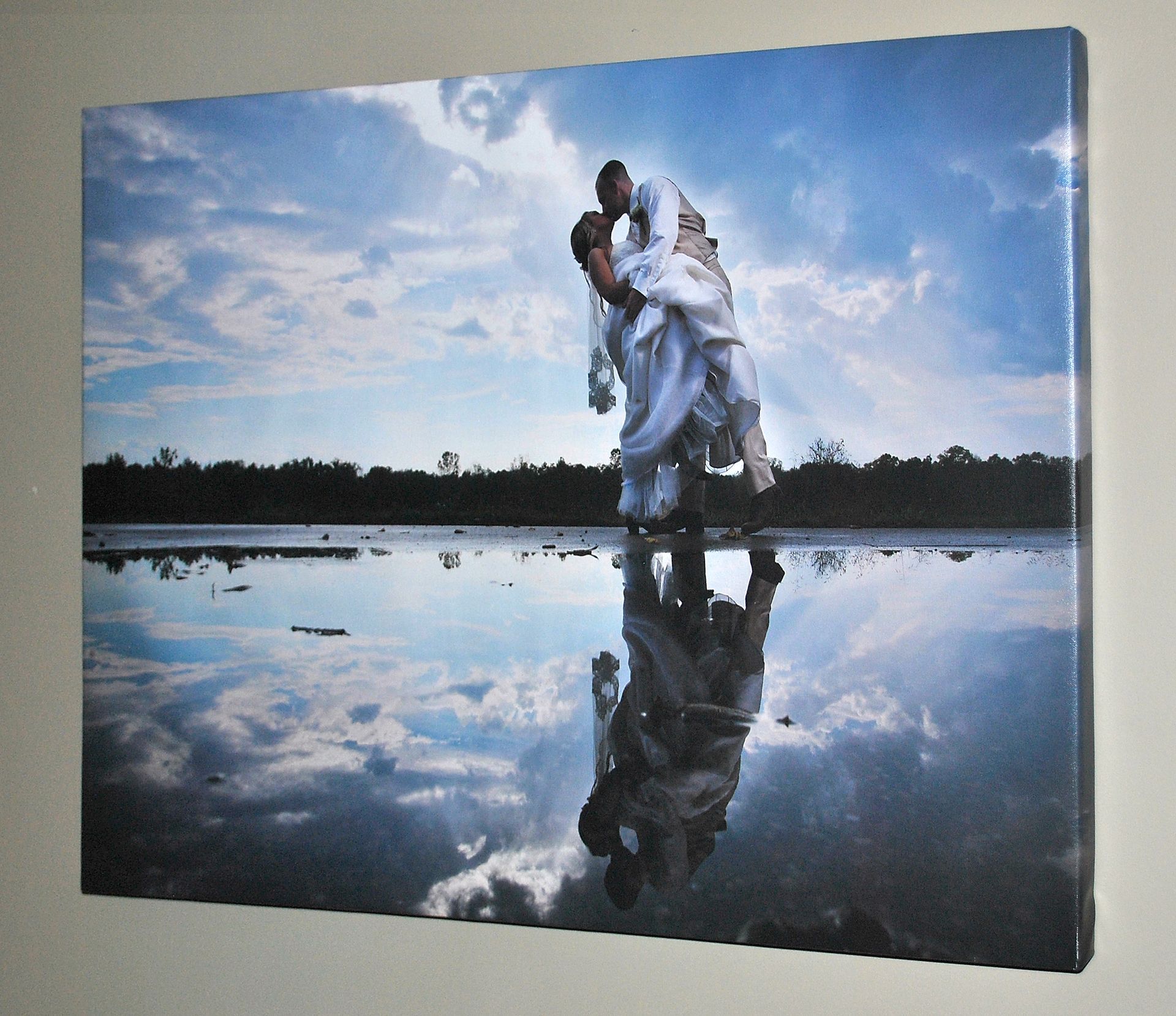 Wedding couple dip in reflective water; sky and trees reflected, blue and white.