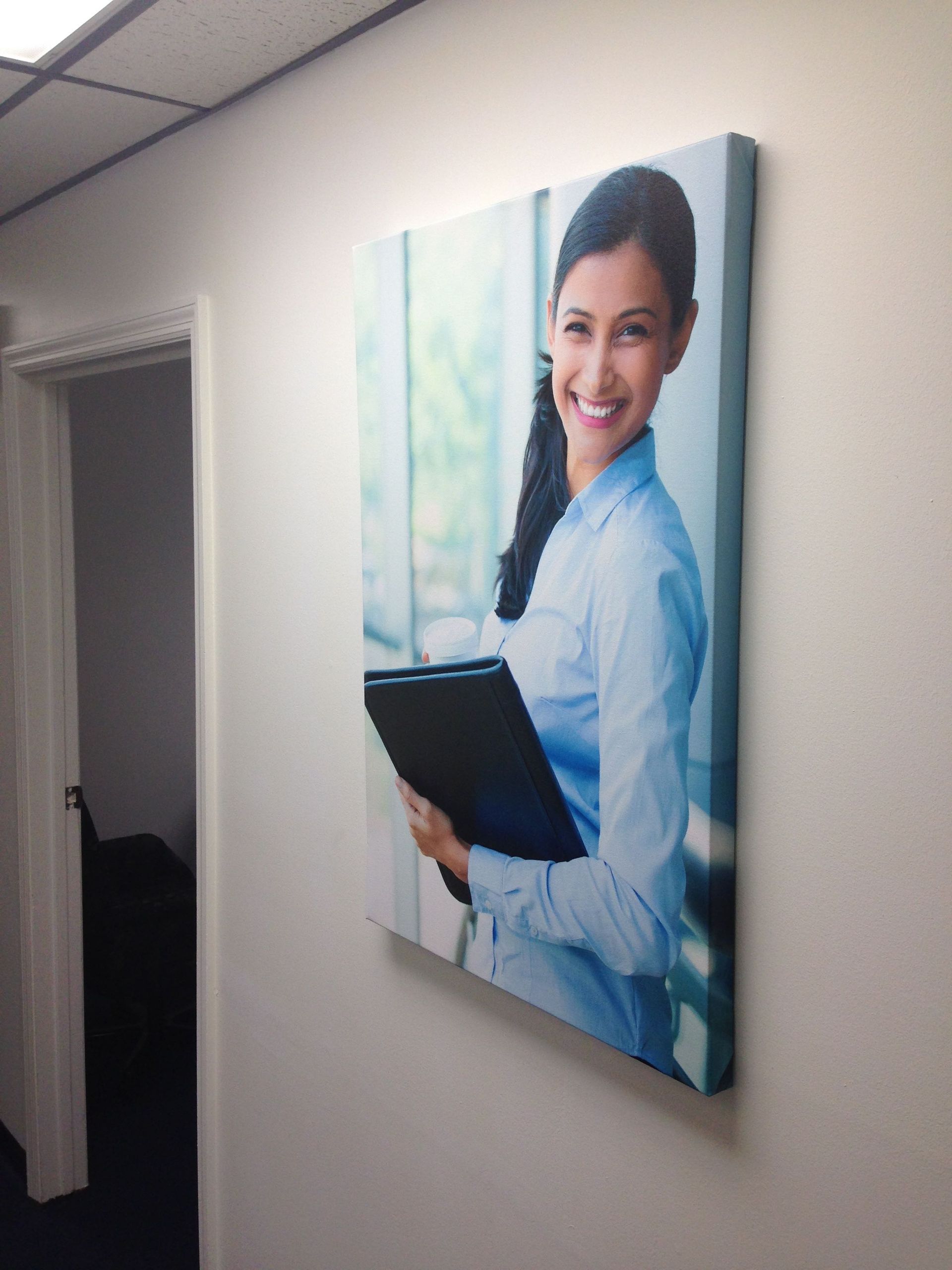 Woman in blue shirt, holding folder, smiling, displayed as canvas print on white office wall.