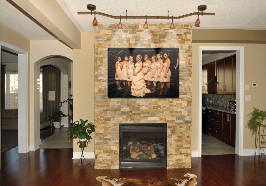 Fireplace with stone surround, TV, and wedding party photo; adjacent kitchen and living areas.