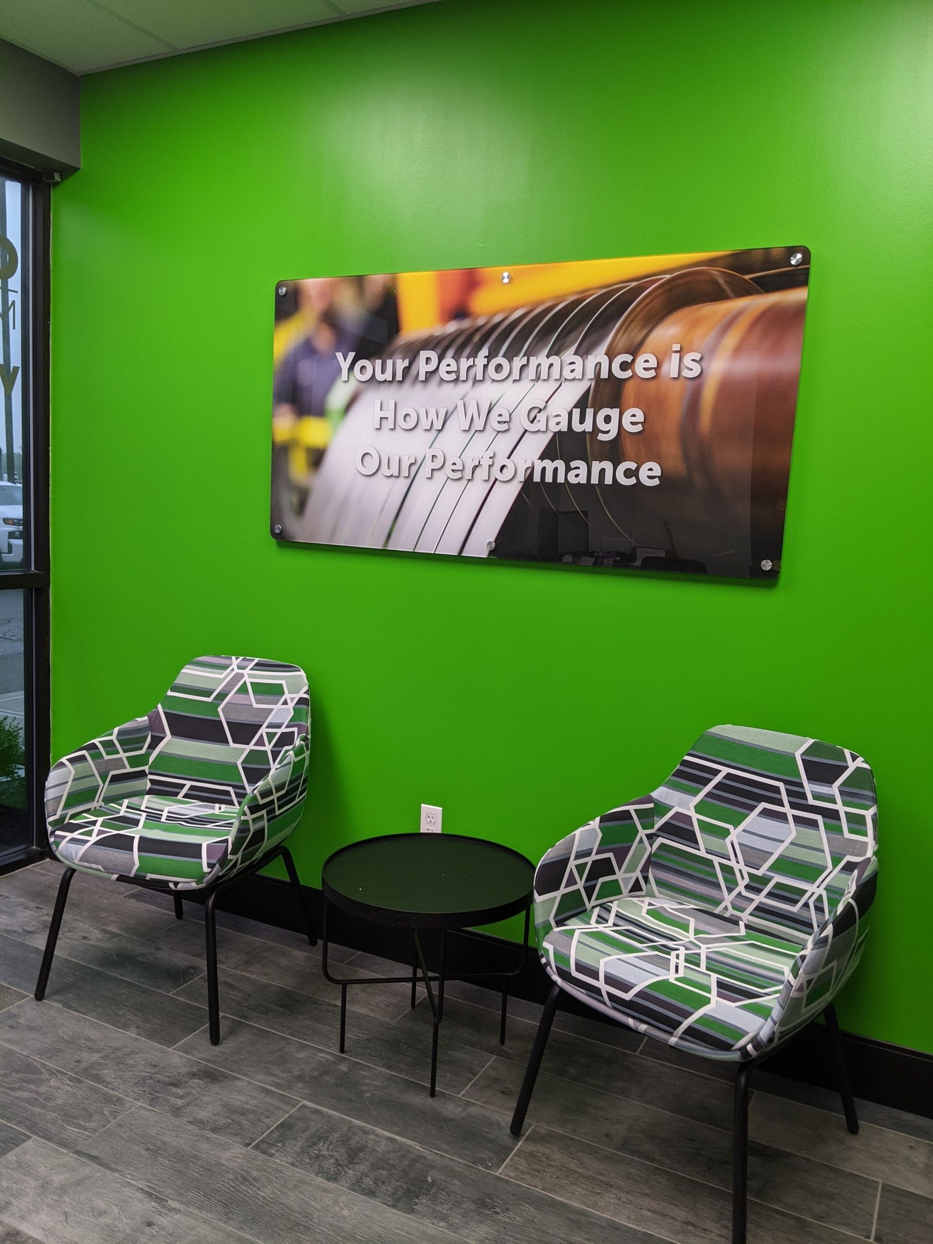 Two patterned chairs, small table, and sign against green wall in a waiting area.