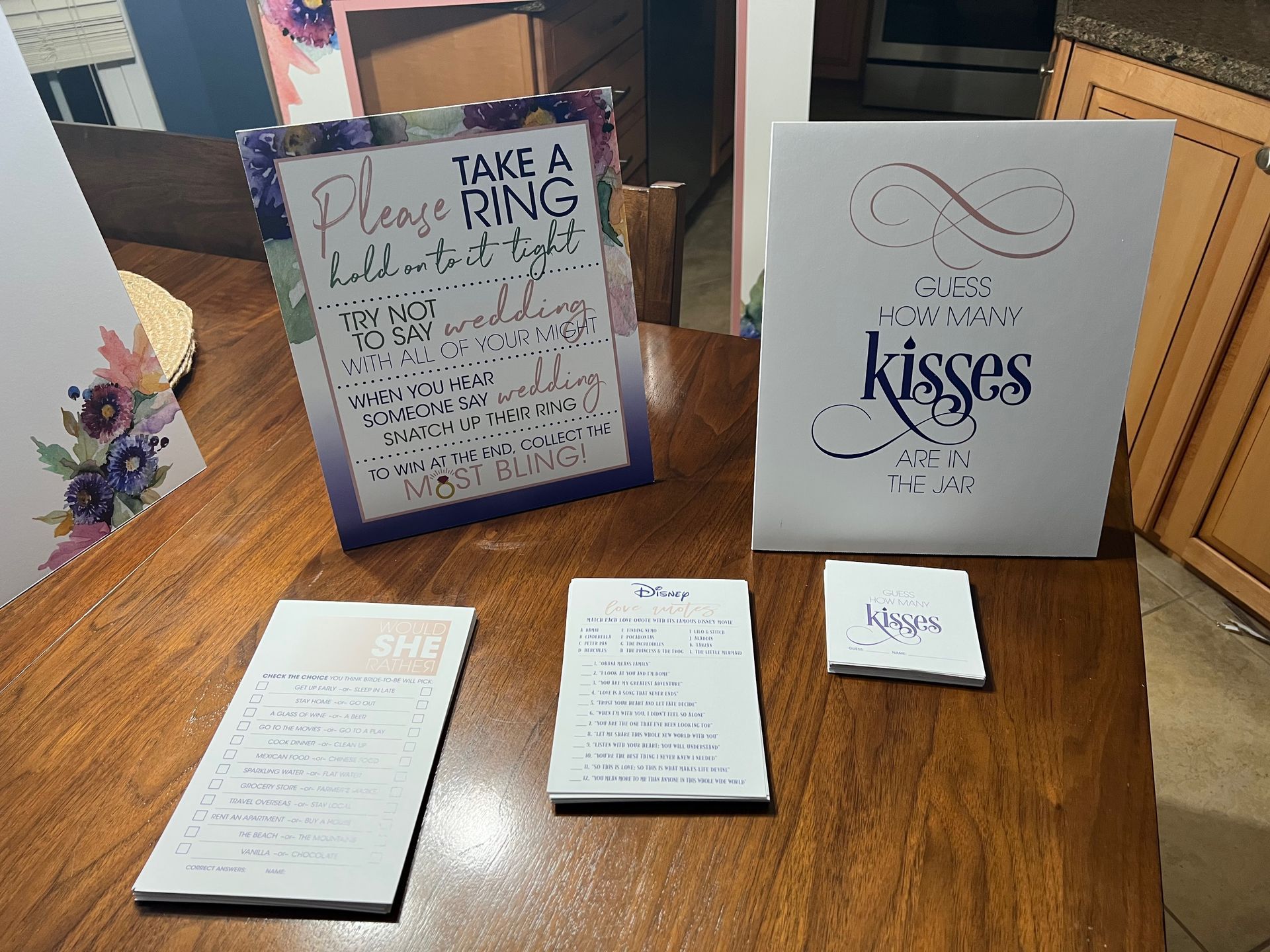 Wedding signage: “Take a Ring” and “sweetest kisses” signs on a wooden table with notepads.