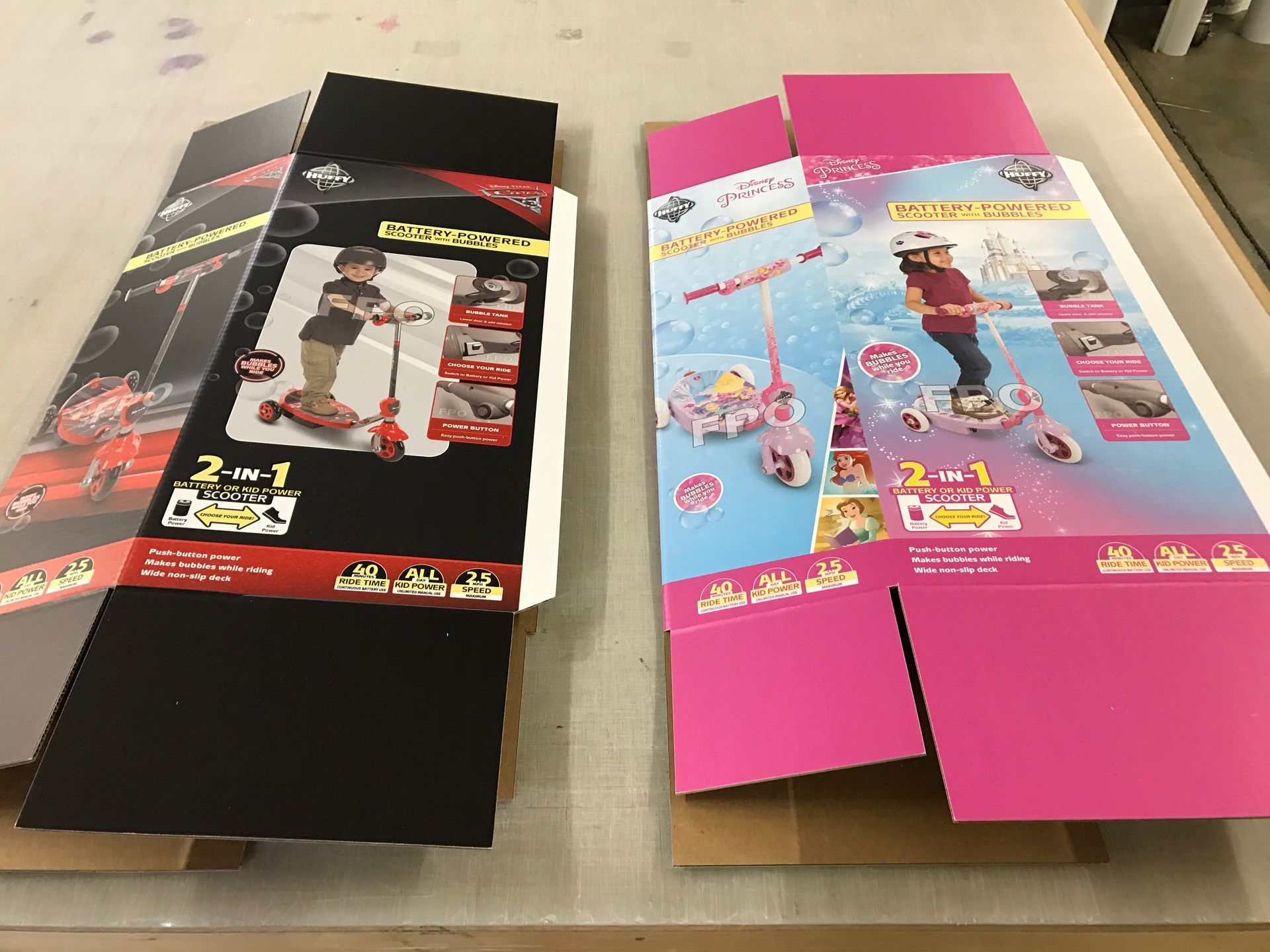 Two folded cardboard boxes, one black and one pink, for children's scooters, showing product images and branding.