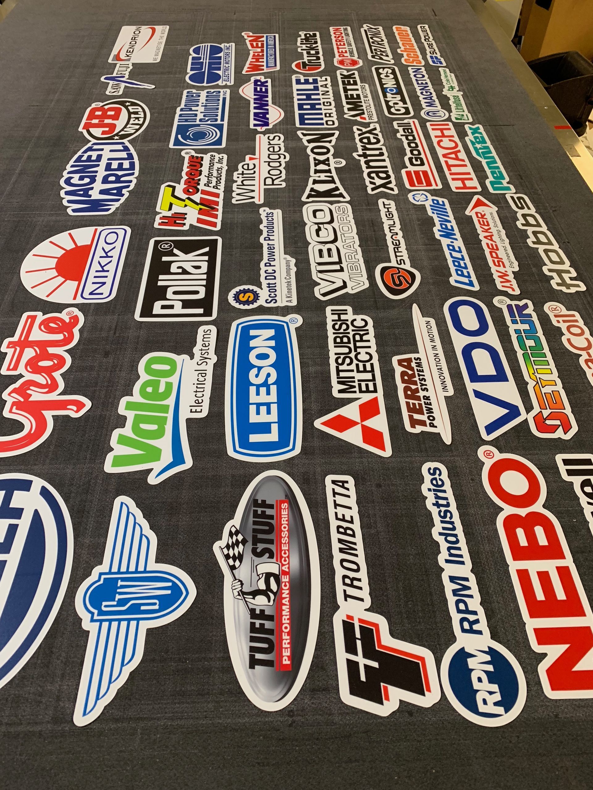 A collection of various brand stickers laid out on a gray surface, including automotive and industrial brands.