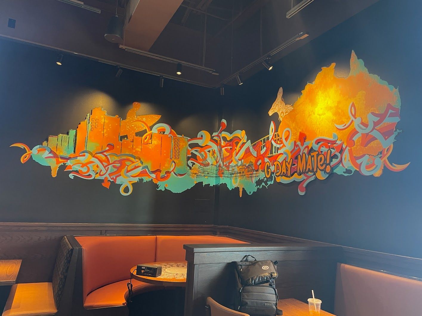 Mural on black wall with orange, green, and white graffiti in a booth setting.