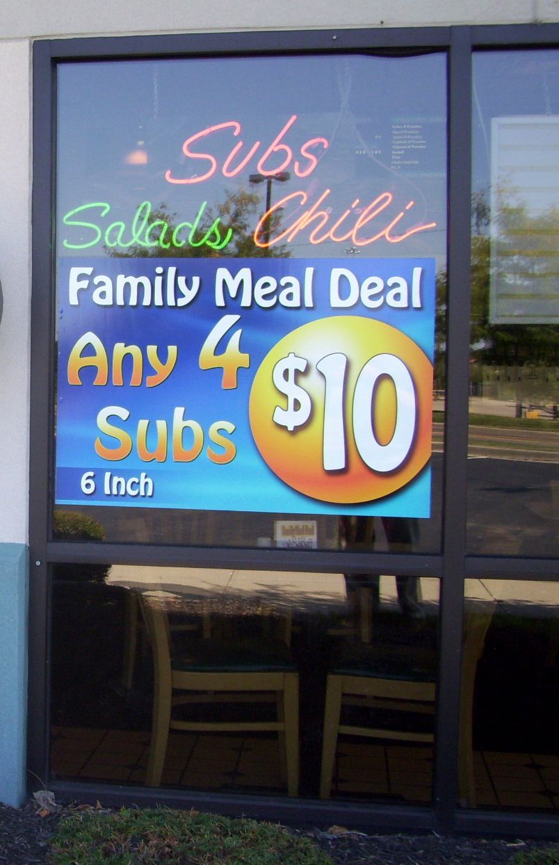 Sign in a window advertising subs, salads, chili, and a family meal deal: any 4 six-inch subs for $10.