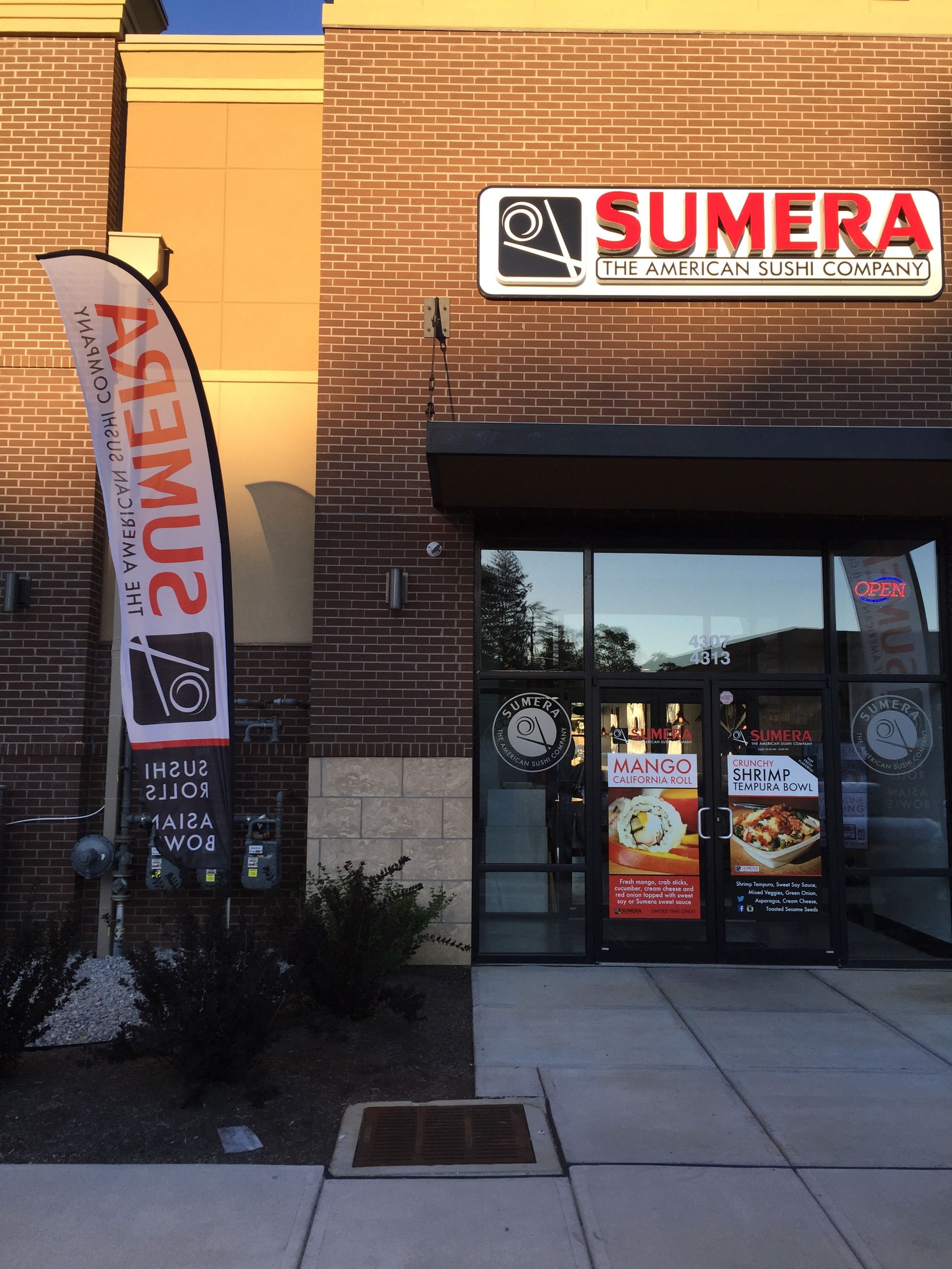 Sumera restaurant storefront with a red brick facade and a promotional flag.