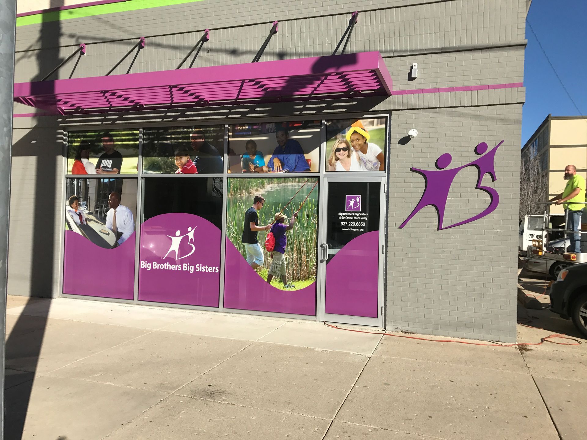 Exterior of a building with purple and white signage for a community center; a person is working on the side.