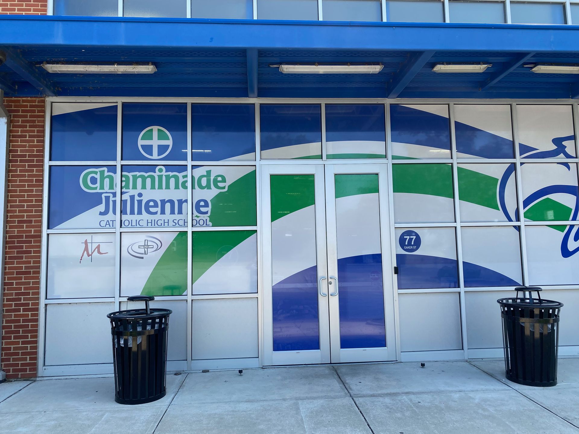 Chaminade Julienne school entrance with blue, green, and white graphics; trash cans in front.