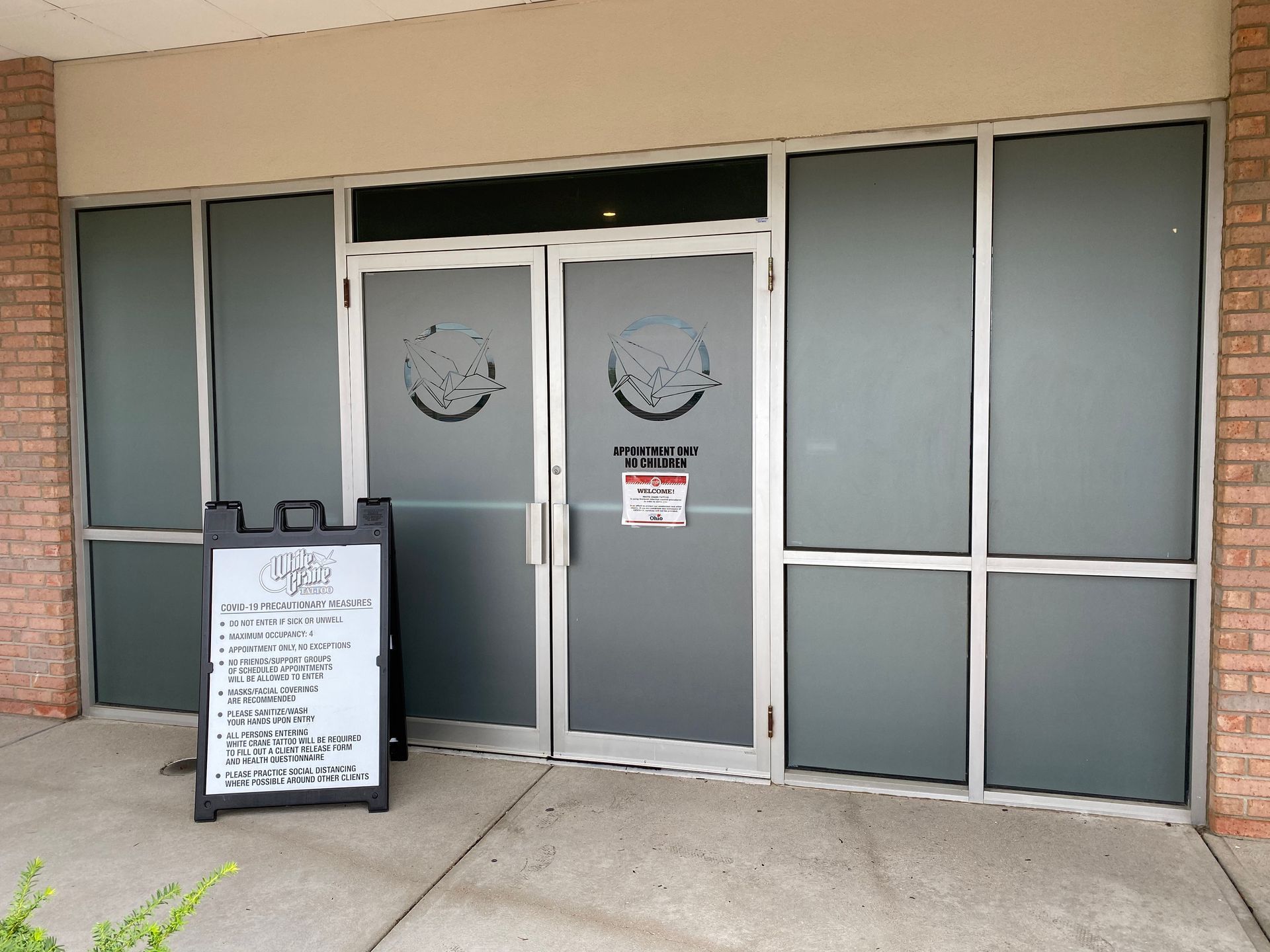 Exterior view of a restaurant with frosted glass doors and windows, an A-frame menu, and brick walls.