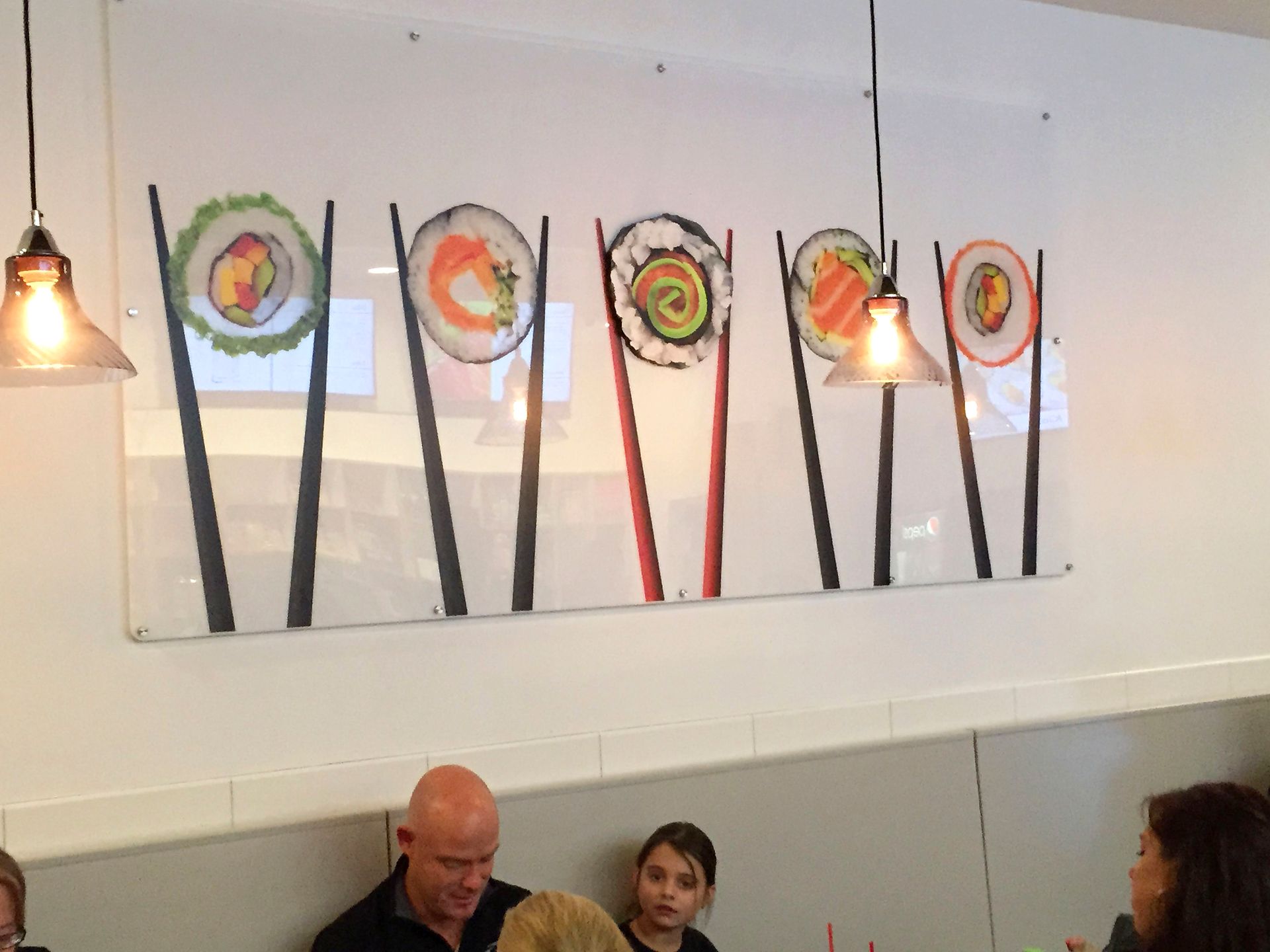 Sushi artwork with chopsticks hanging above patrons in a restaurant.