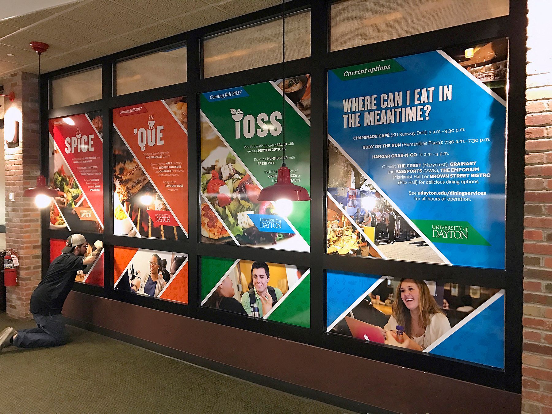 Man installs colorful food service advertisement posters in a brick-walled corridor.