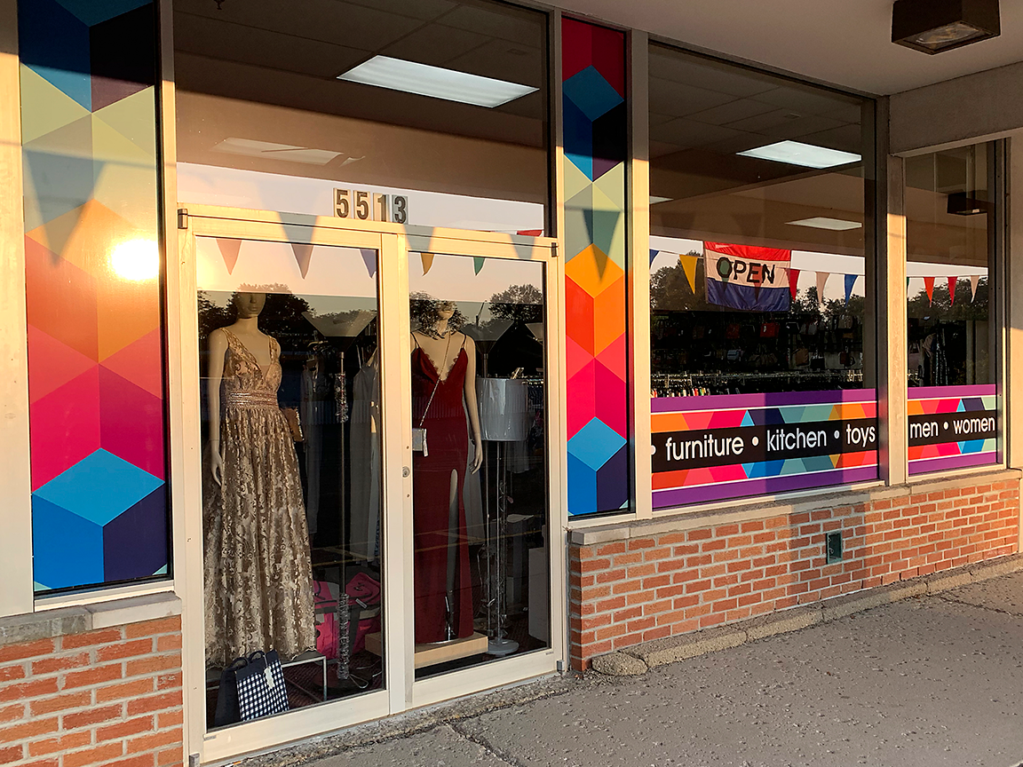 Storefront with colorful geometric window decorations, clothing in the windows, and brick exterior.