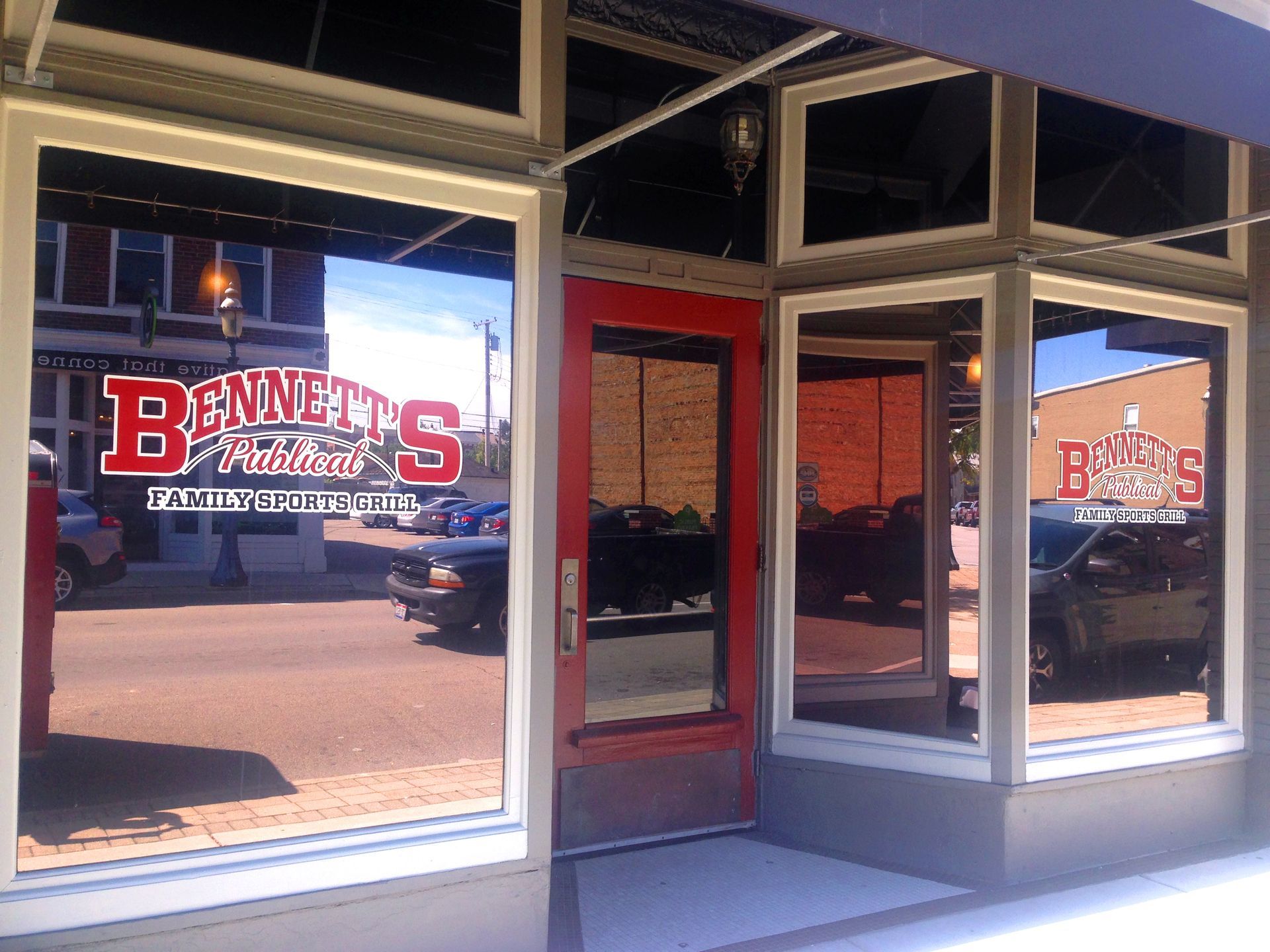 Bennett's Kitchen storefront with reflective windows, red door, and logo visible. Exterior street view with cars.